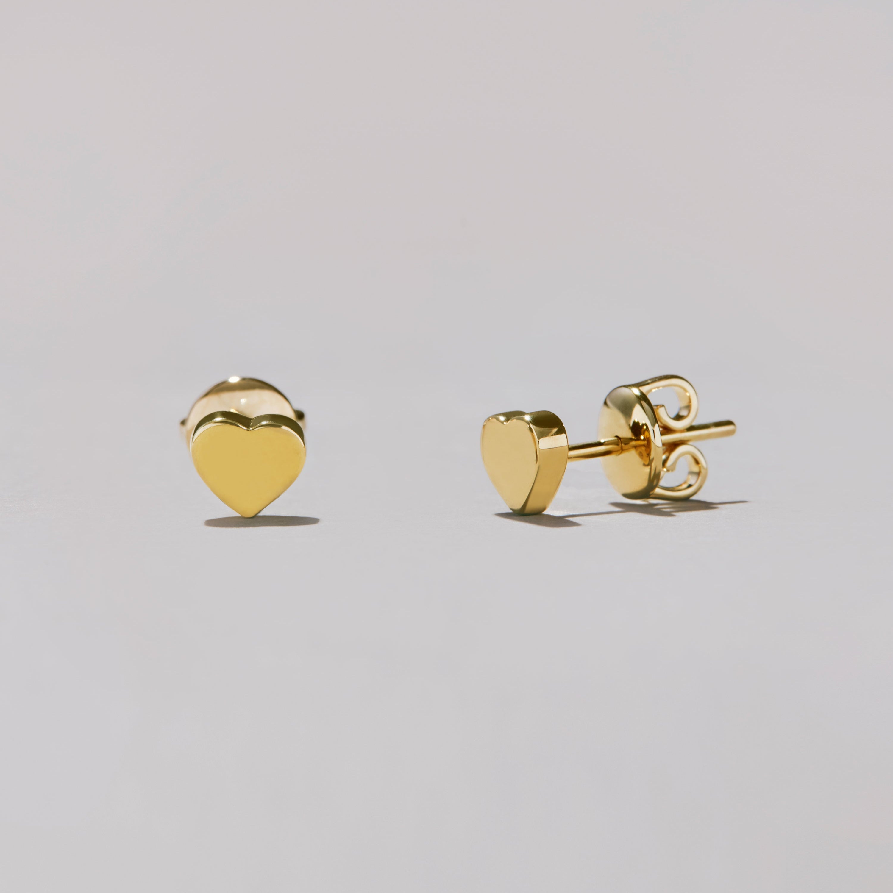 Gold heart-shaped stud earrings on a light gray background