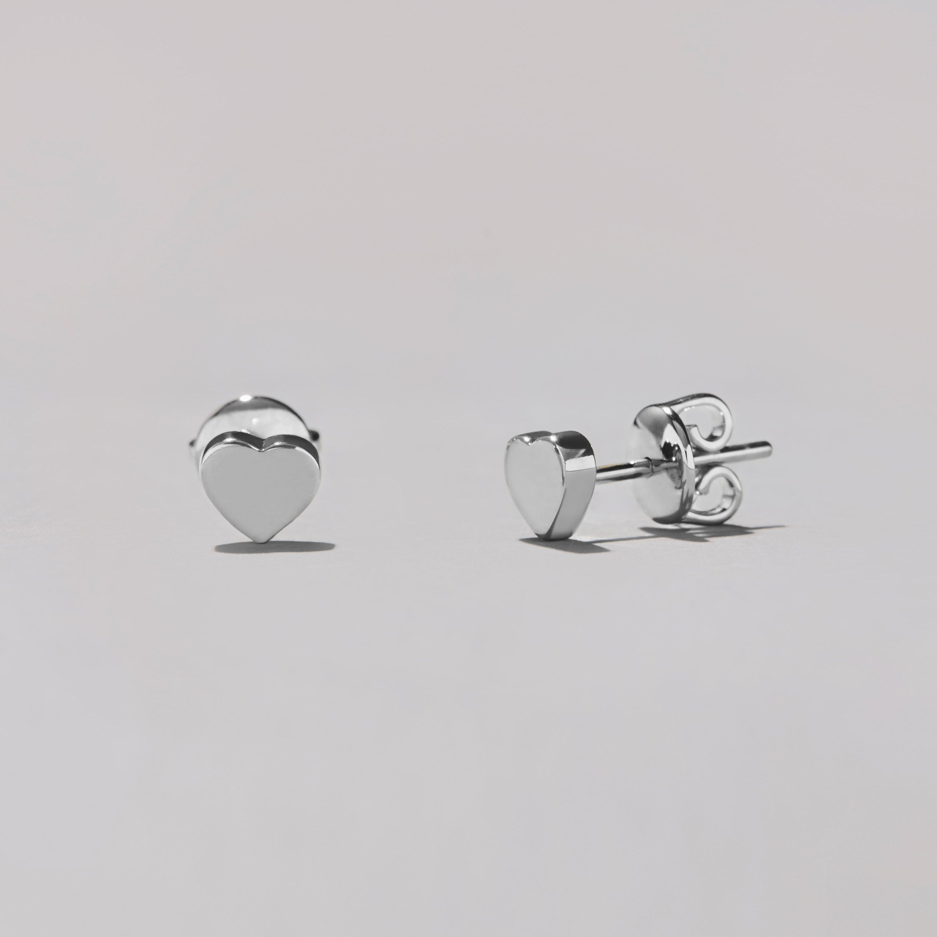 Heart-shaped silver stud earrings on a light gray background