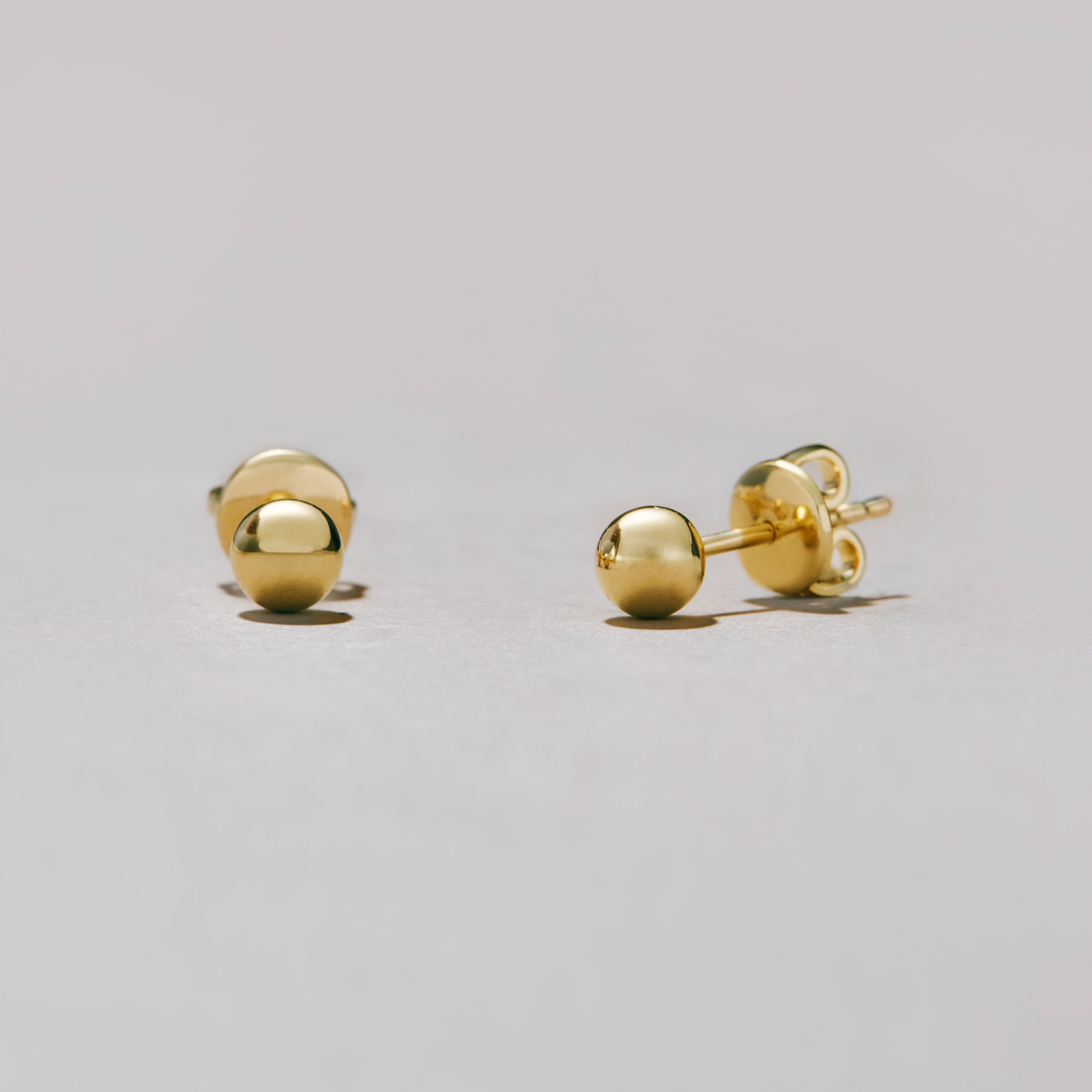 Gold ball earrings on a light gray background