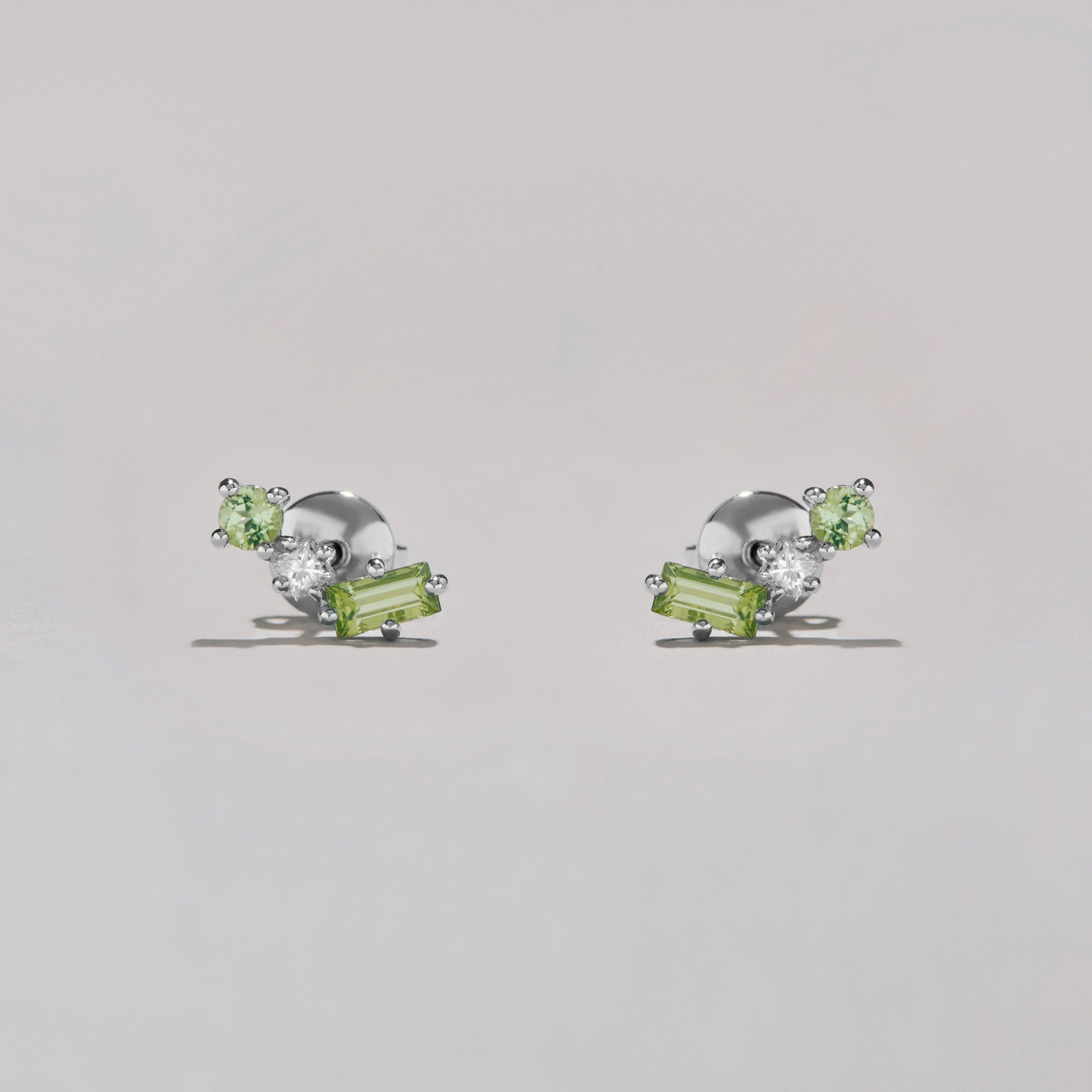 Pair of silver earrings with green and clear gemstones on a light gray background