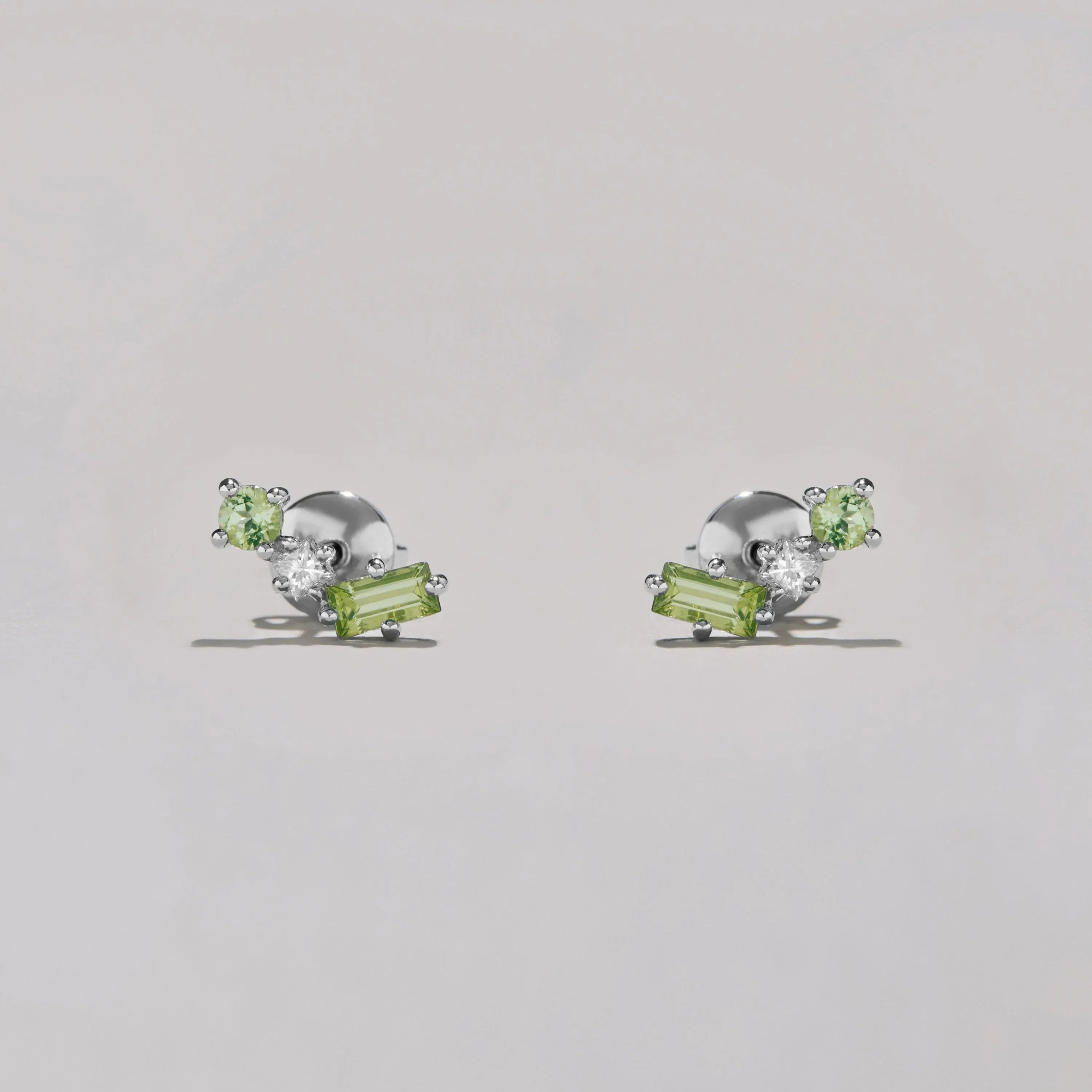 Pair of silver earrings with green and clear gemstones on a light gray background