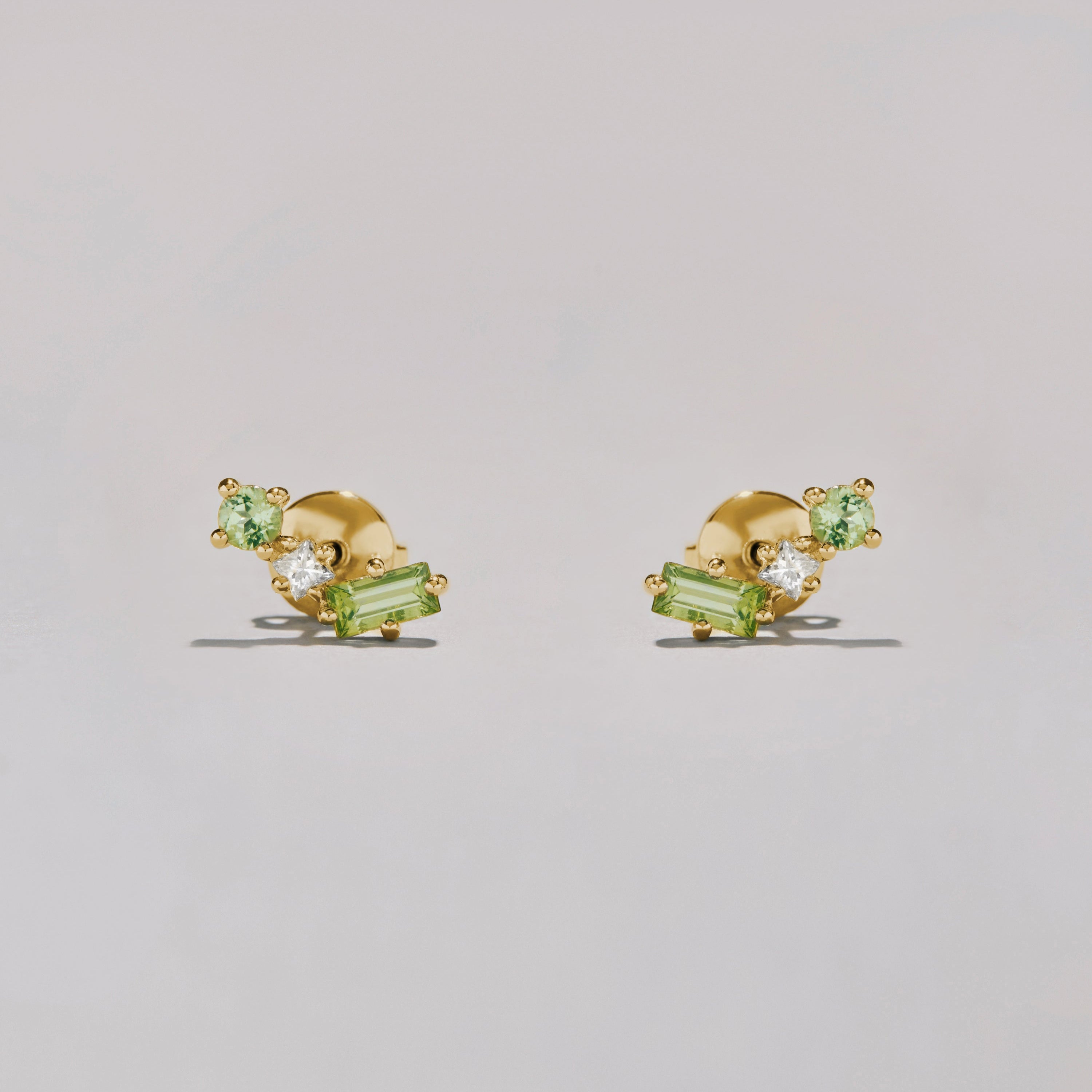 Gold earrings with green and clear gemstones on a light gray background