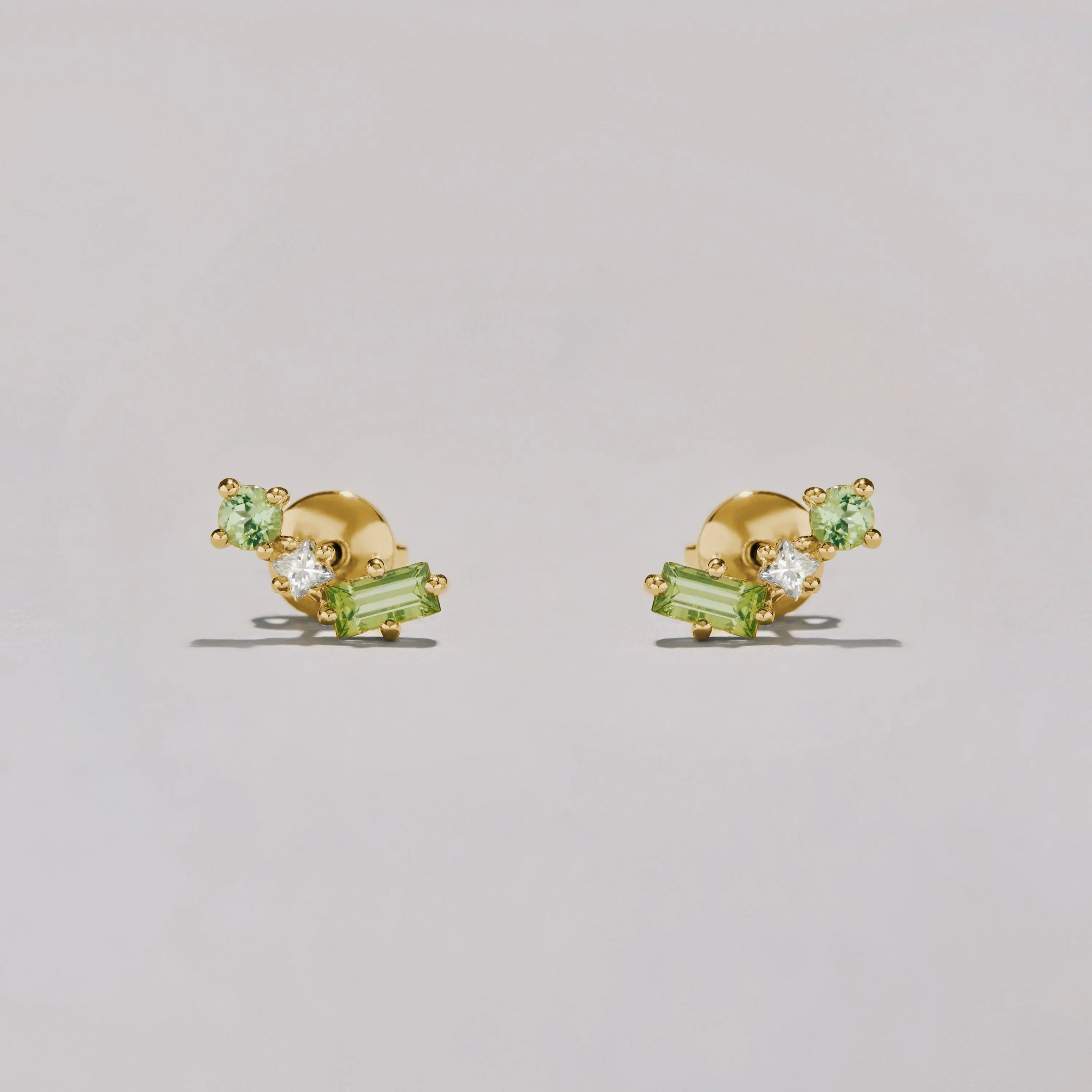 Gold earrings with green and clear gemstones on a light gray background