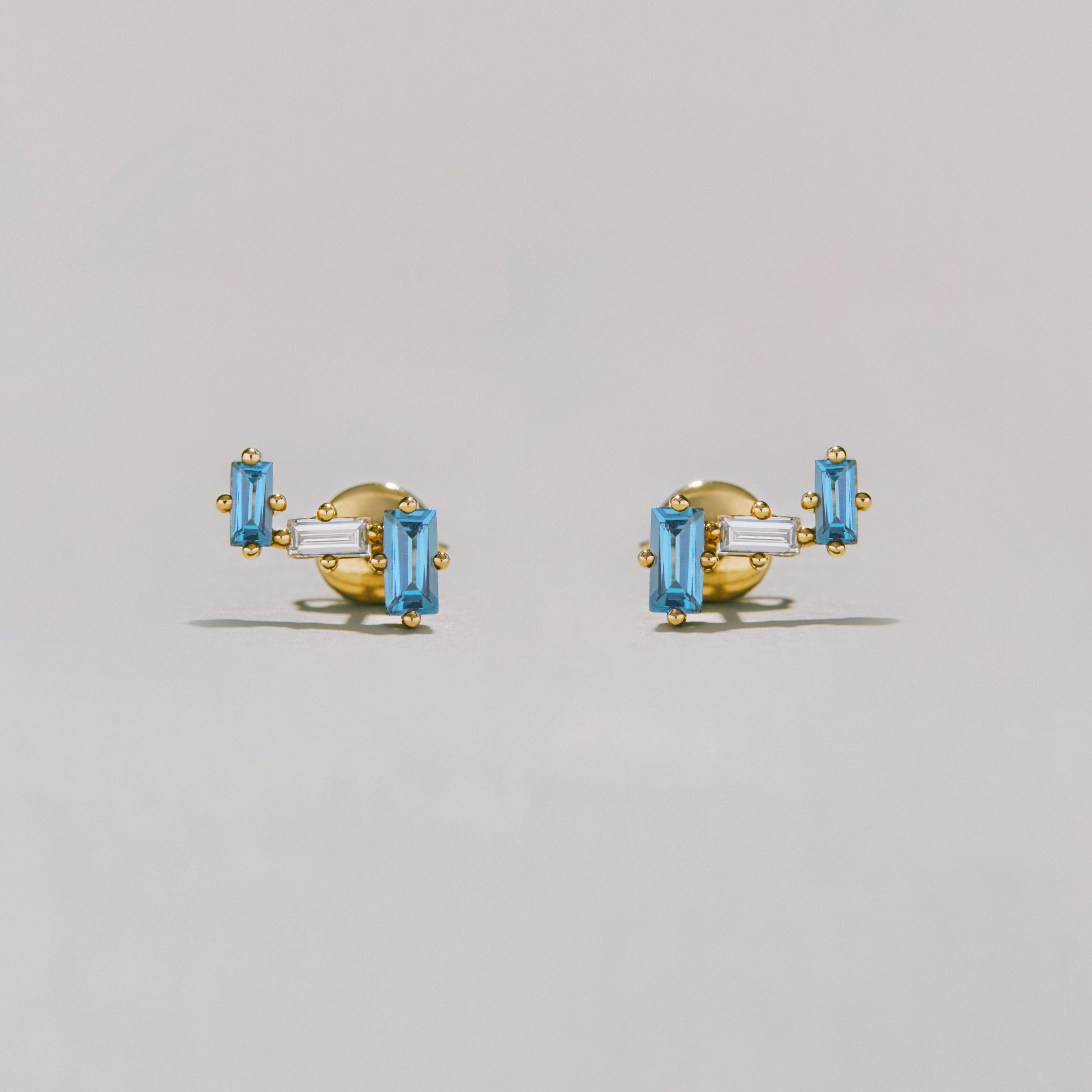 Gold earrings with clear and blue gemstones on a light gray background