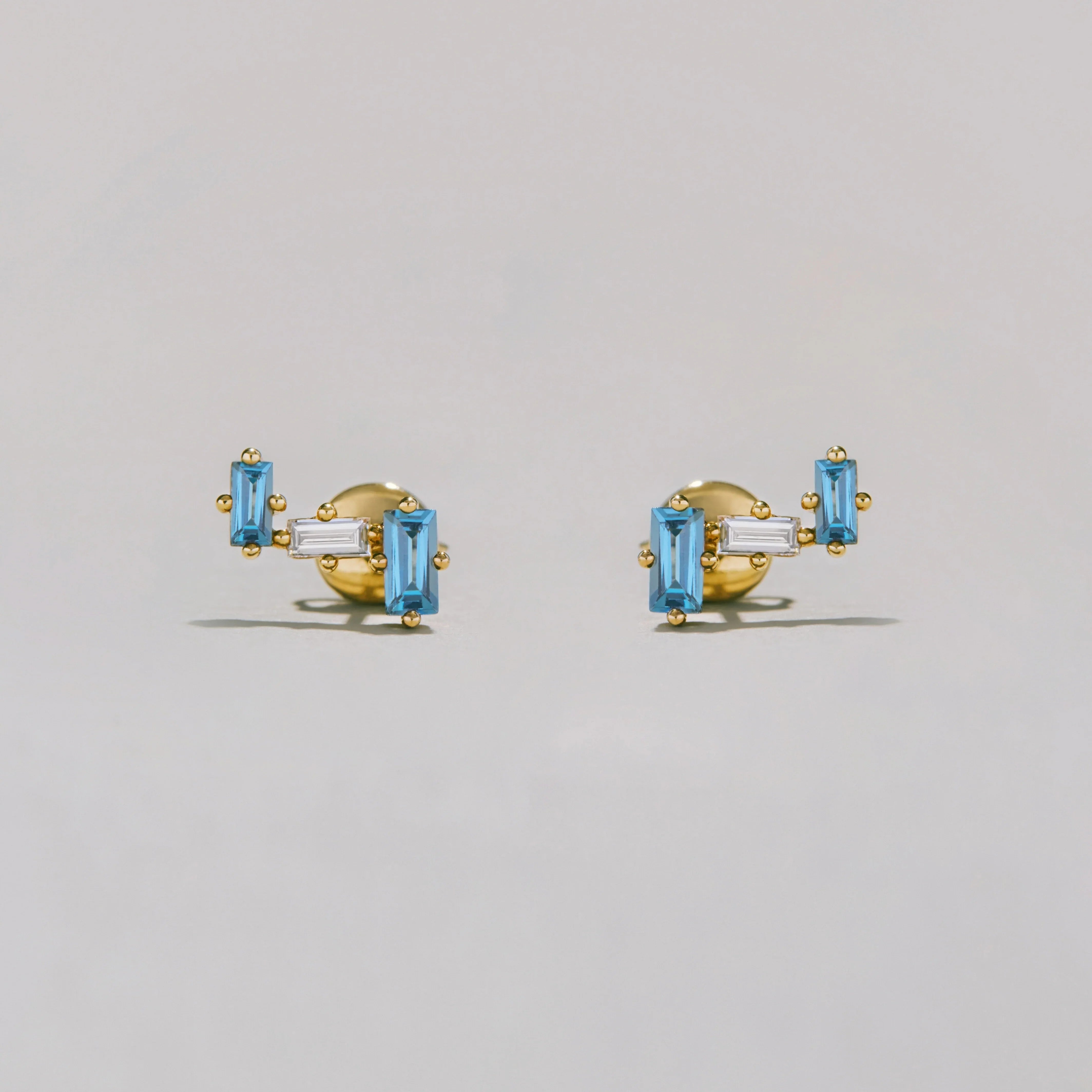 Gold earrings with clear and blue gemstones on a light gray background