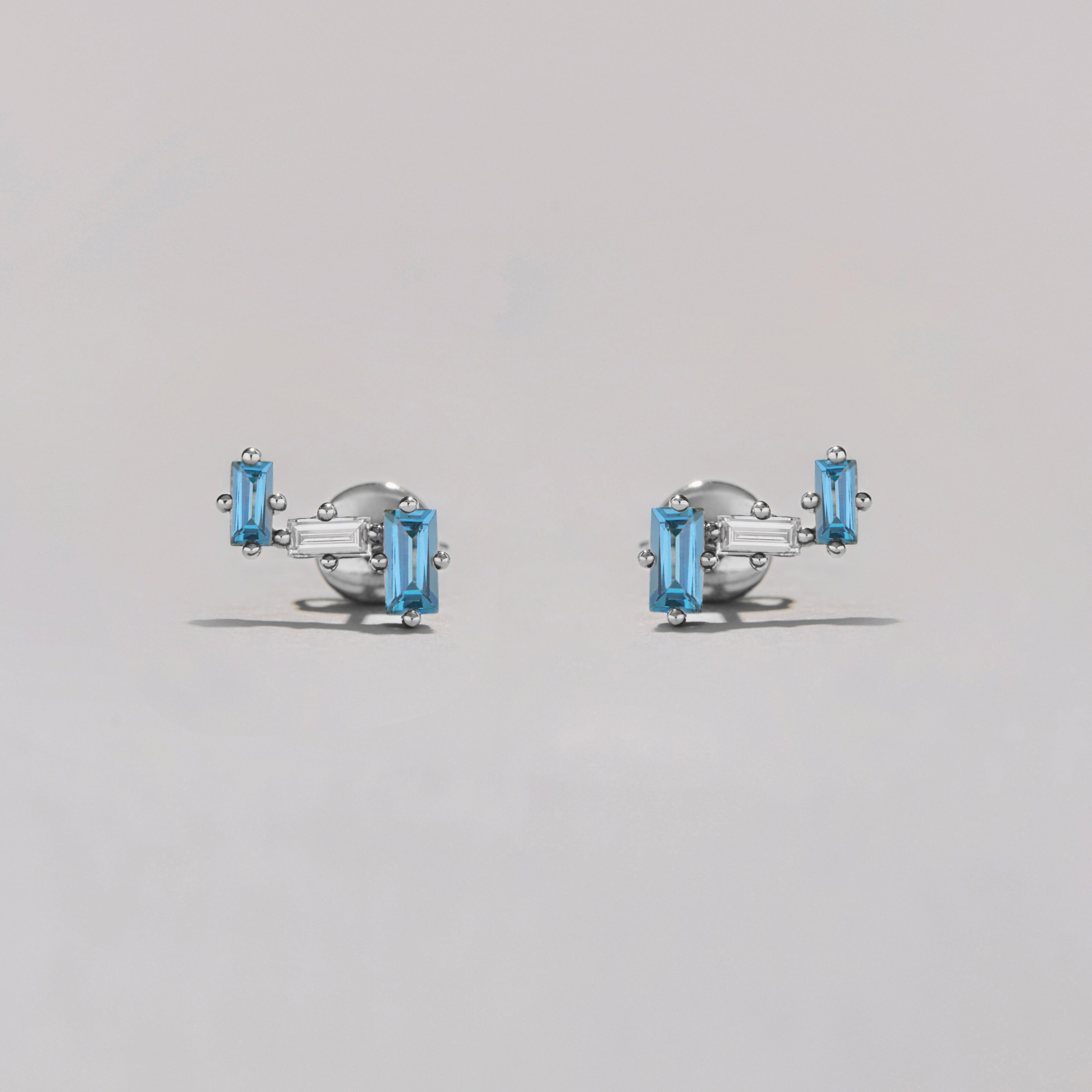 Pair of silver earrings with clear and blue gemstones on a gray background