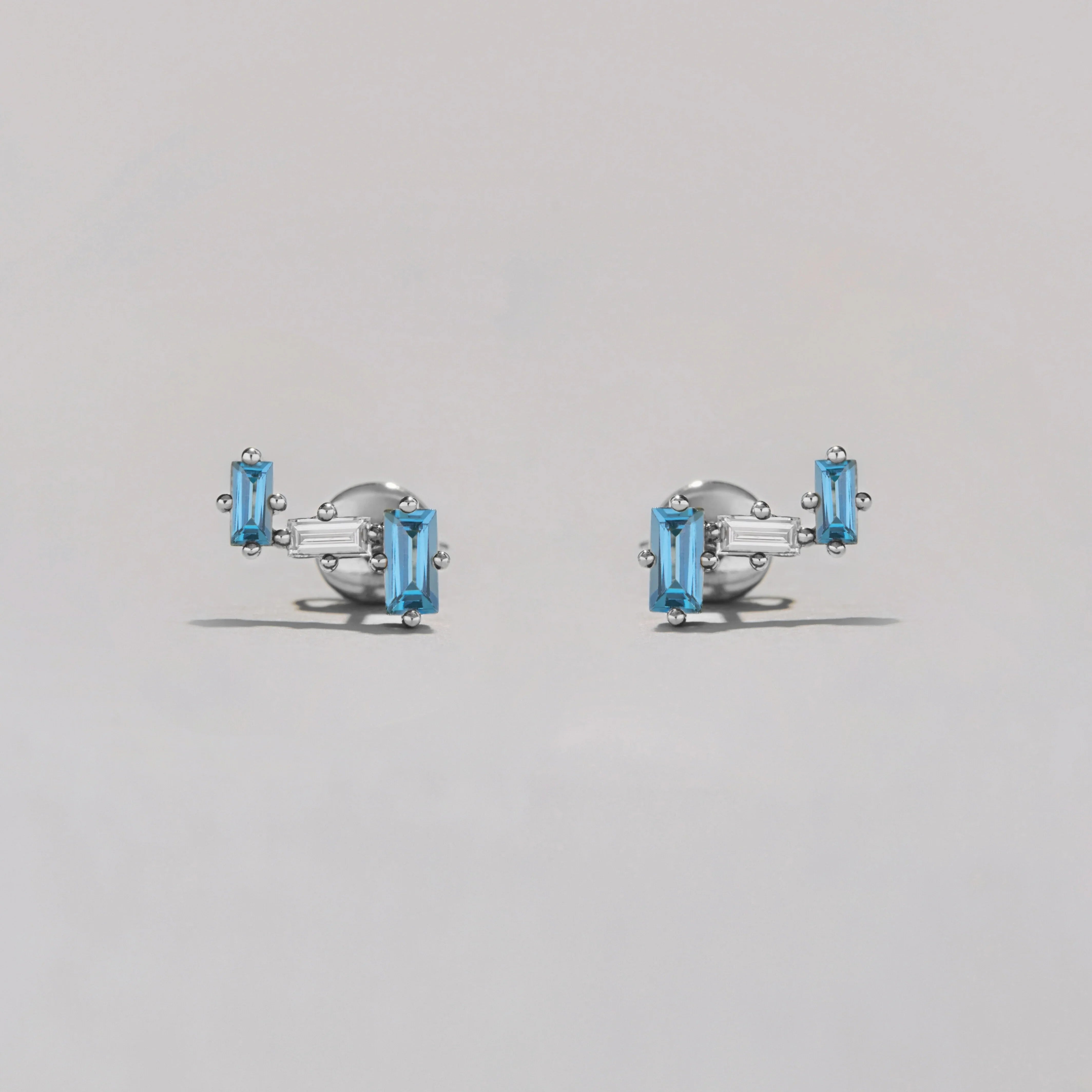Pair of silver earrings with clear and blue gemstones on a gray background