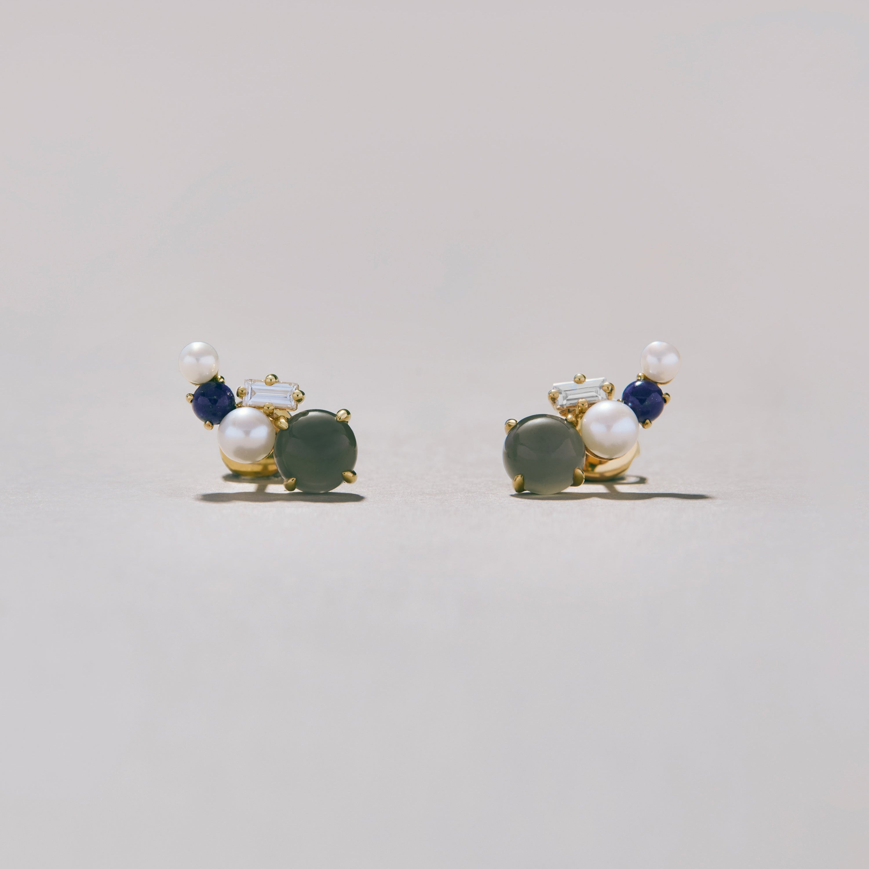 Pair of gold earrings with pearls and gemstones on a light gray background