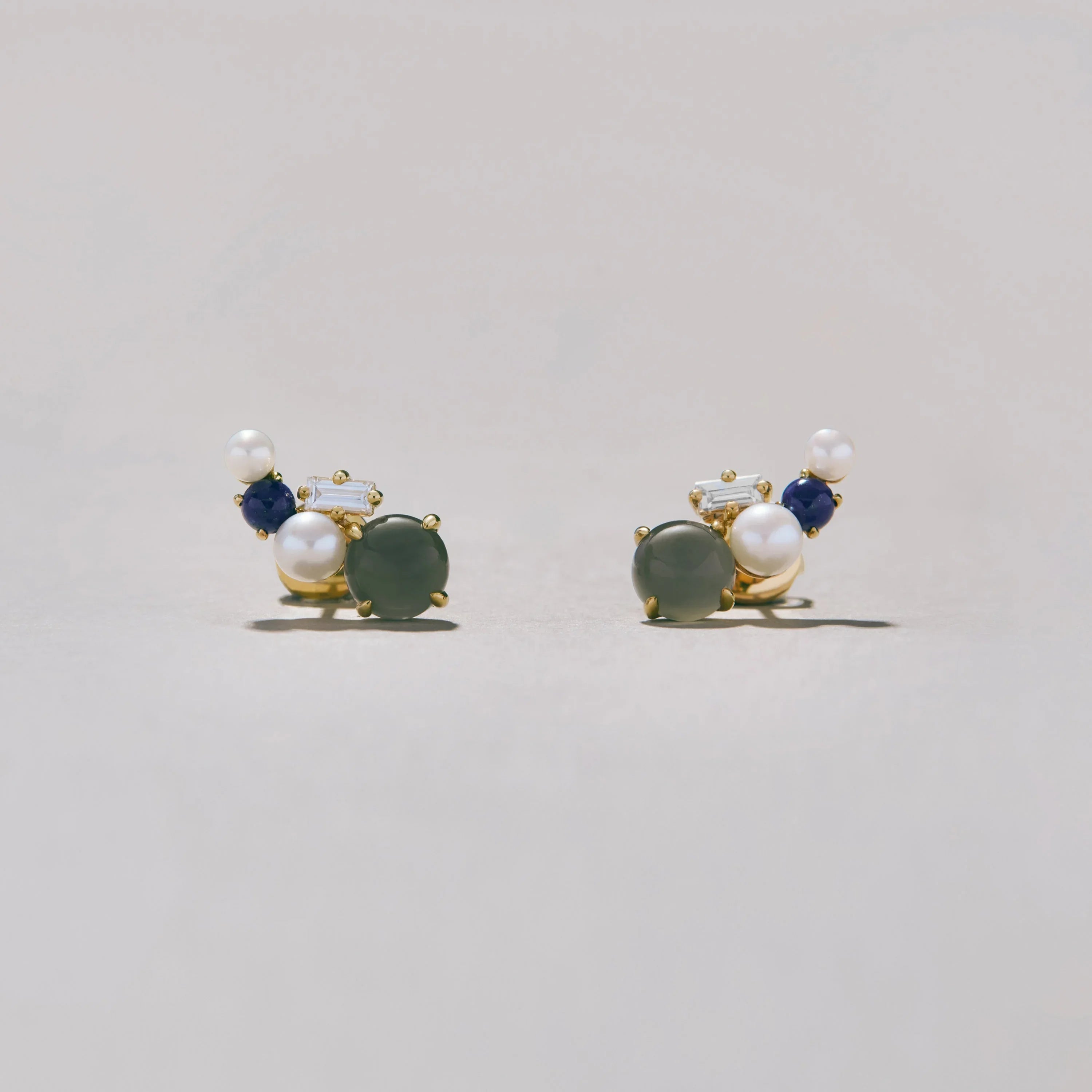 Pair of gold earrings with pearls and gemstones on a light gray background