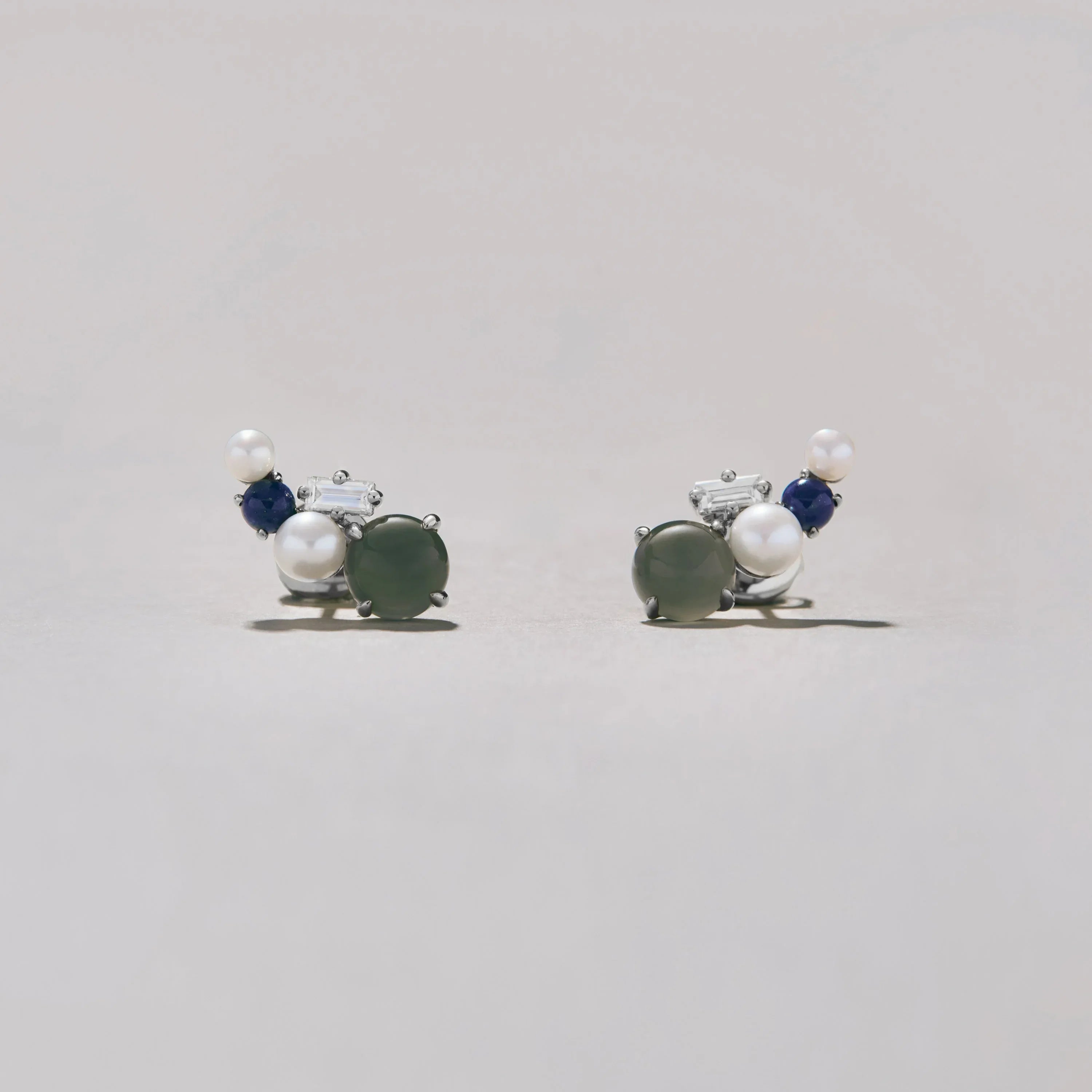 Pair of silver earrings with pearls and blue stones on a light gray background