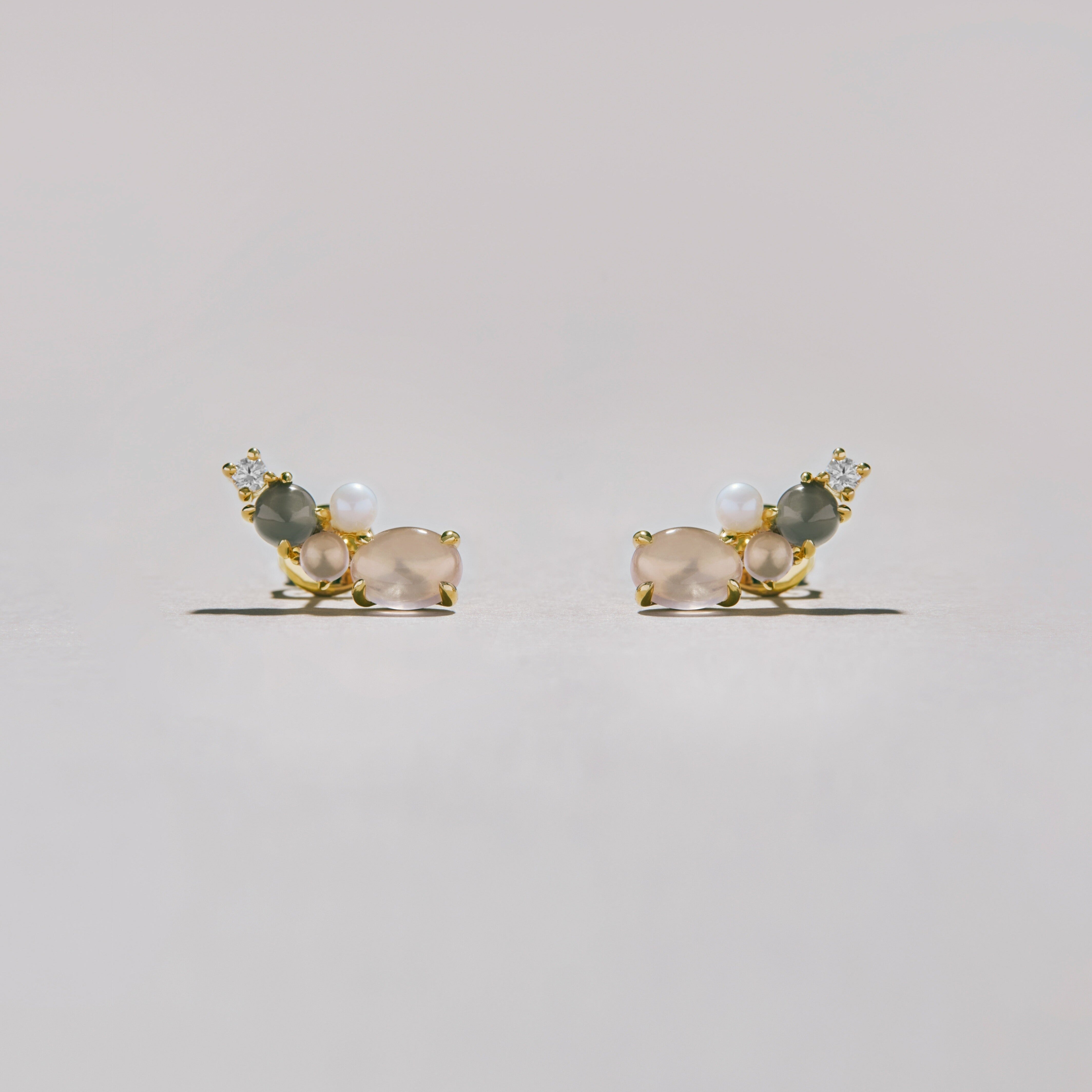 Pair of gold cluster stud earrings with soft pink and gray moonstones, pearls, and crystals, styled on light surface.