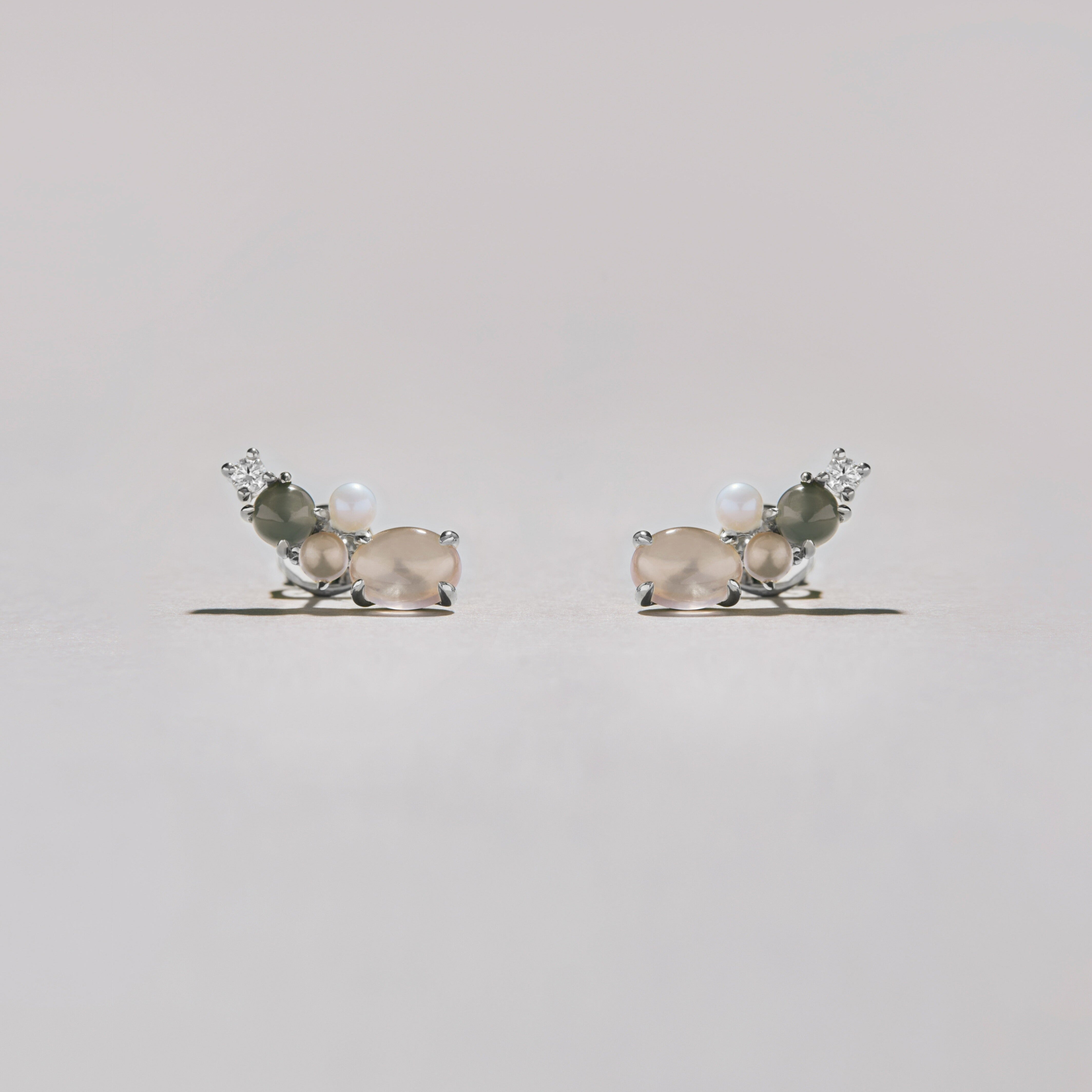 Pair of silver cluster stud earrings with soft pink and gray moonstones, pearls, and crystals, styled on light surface.