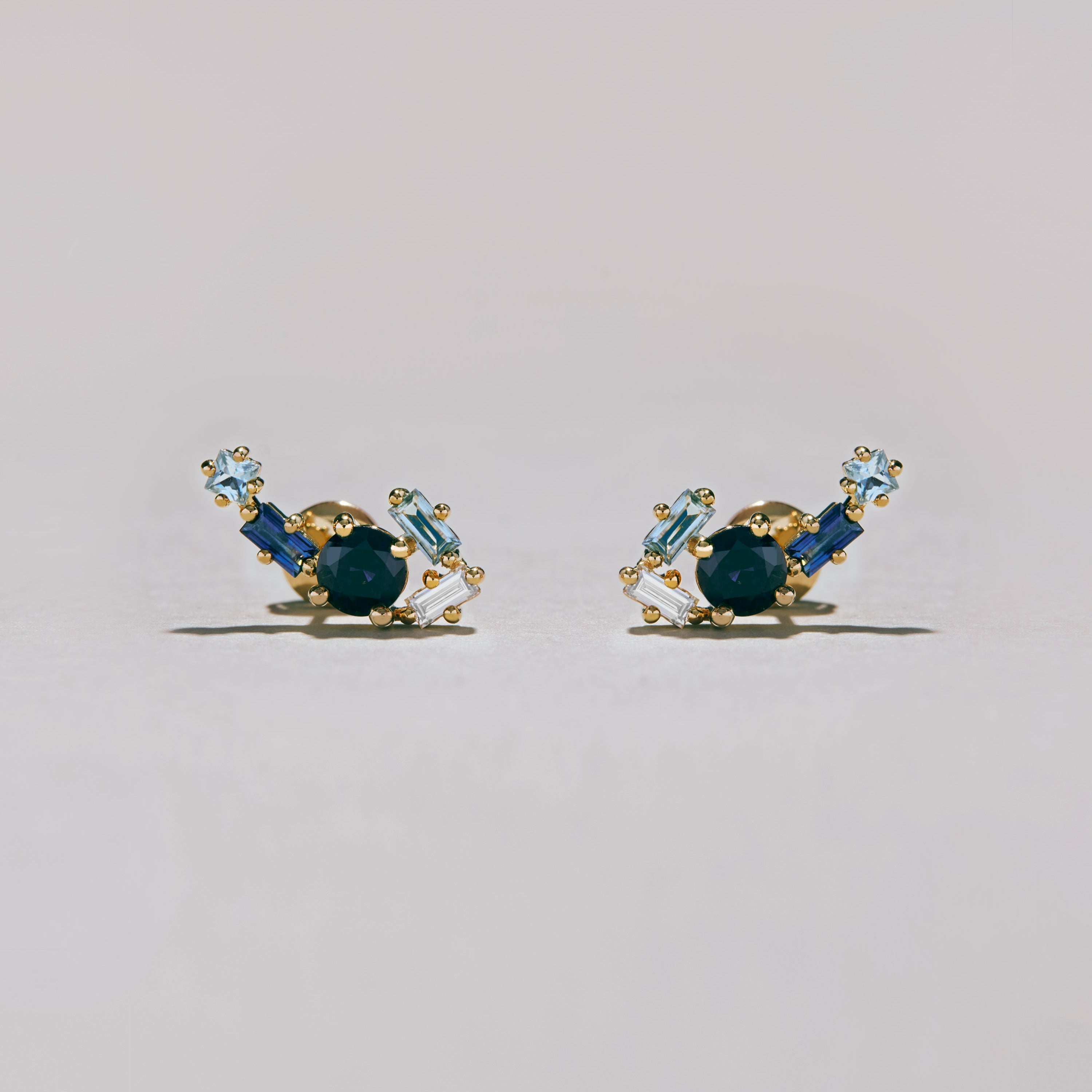 Studio photo of gold blue gemstone cluster earrings with light and dark blue stones on pale background.