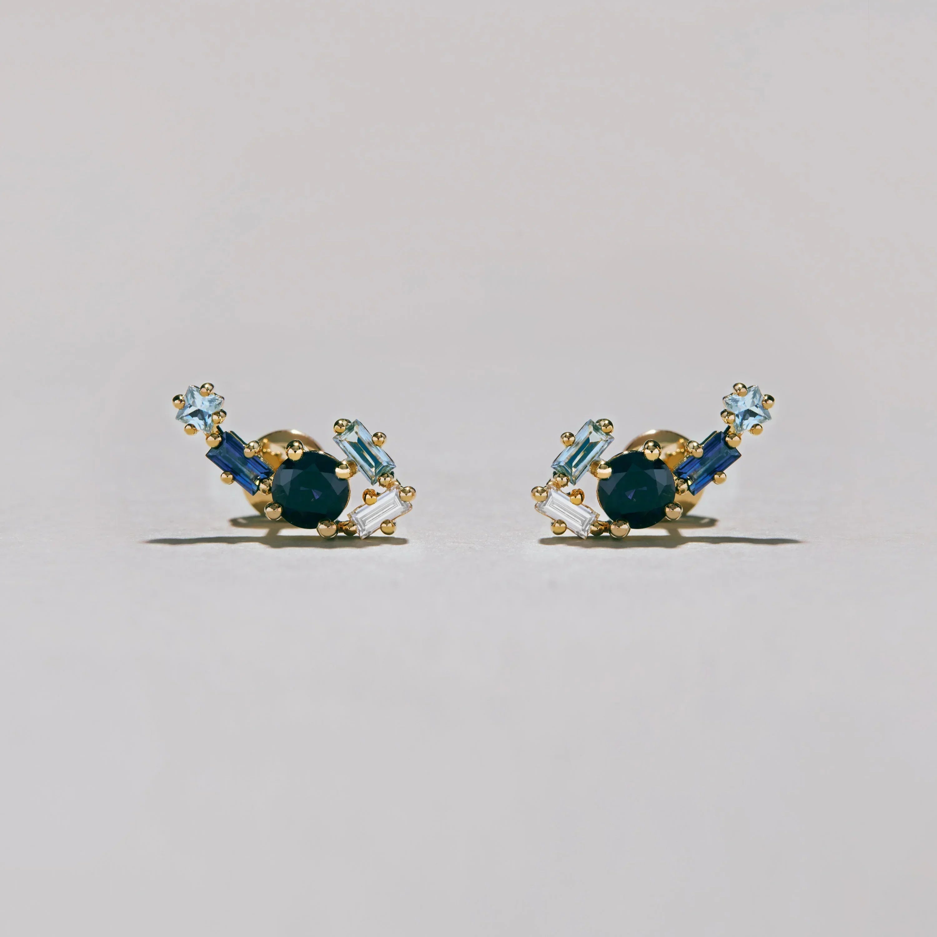 Studio photo of gold blue gemstone cluster earrings with light and dark blue stones on pale background.