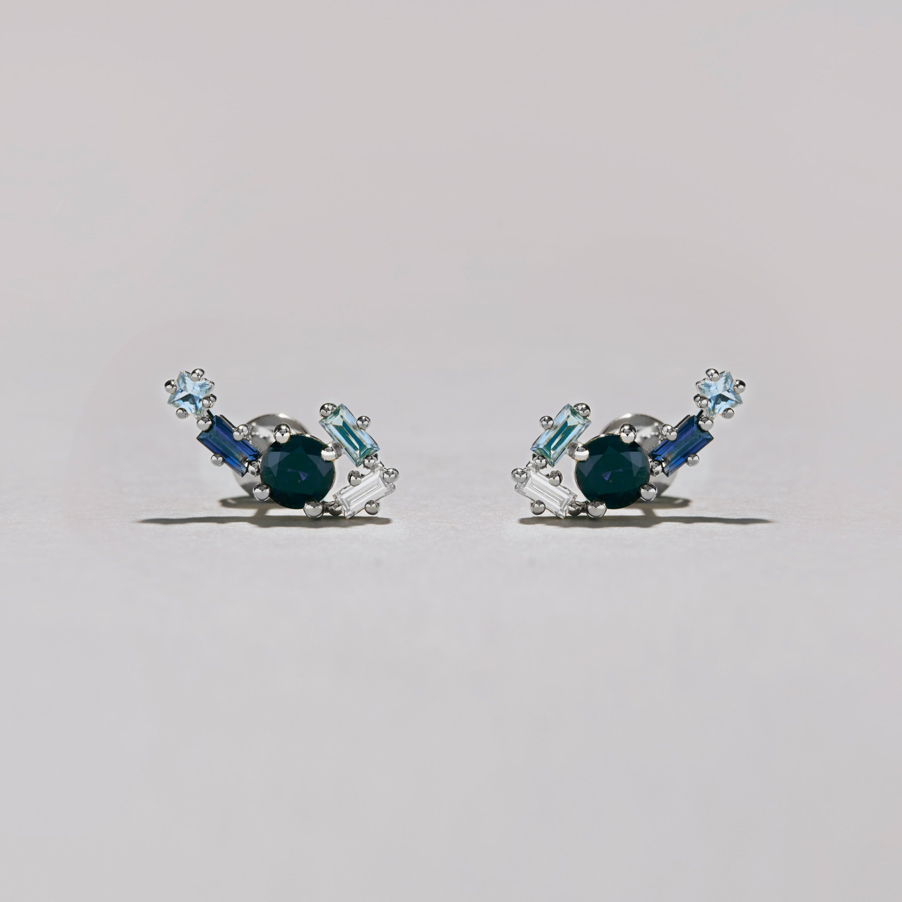 Studio photo of silver blue gemstone cluster earrings with light and dark blue stones on pale background.