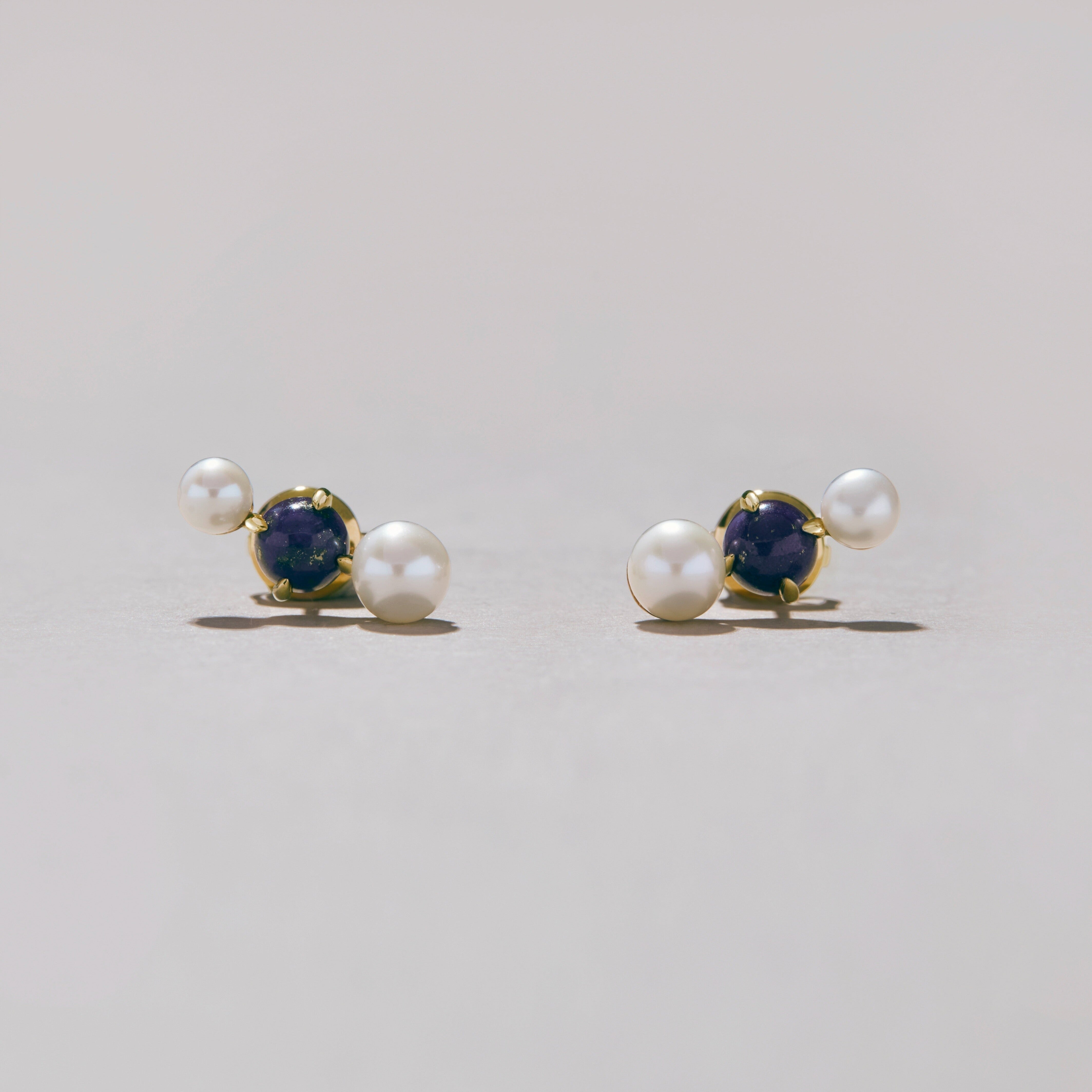 Pair of gold earrings with pearl and blue gemstone on a light gray background