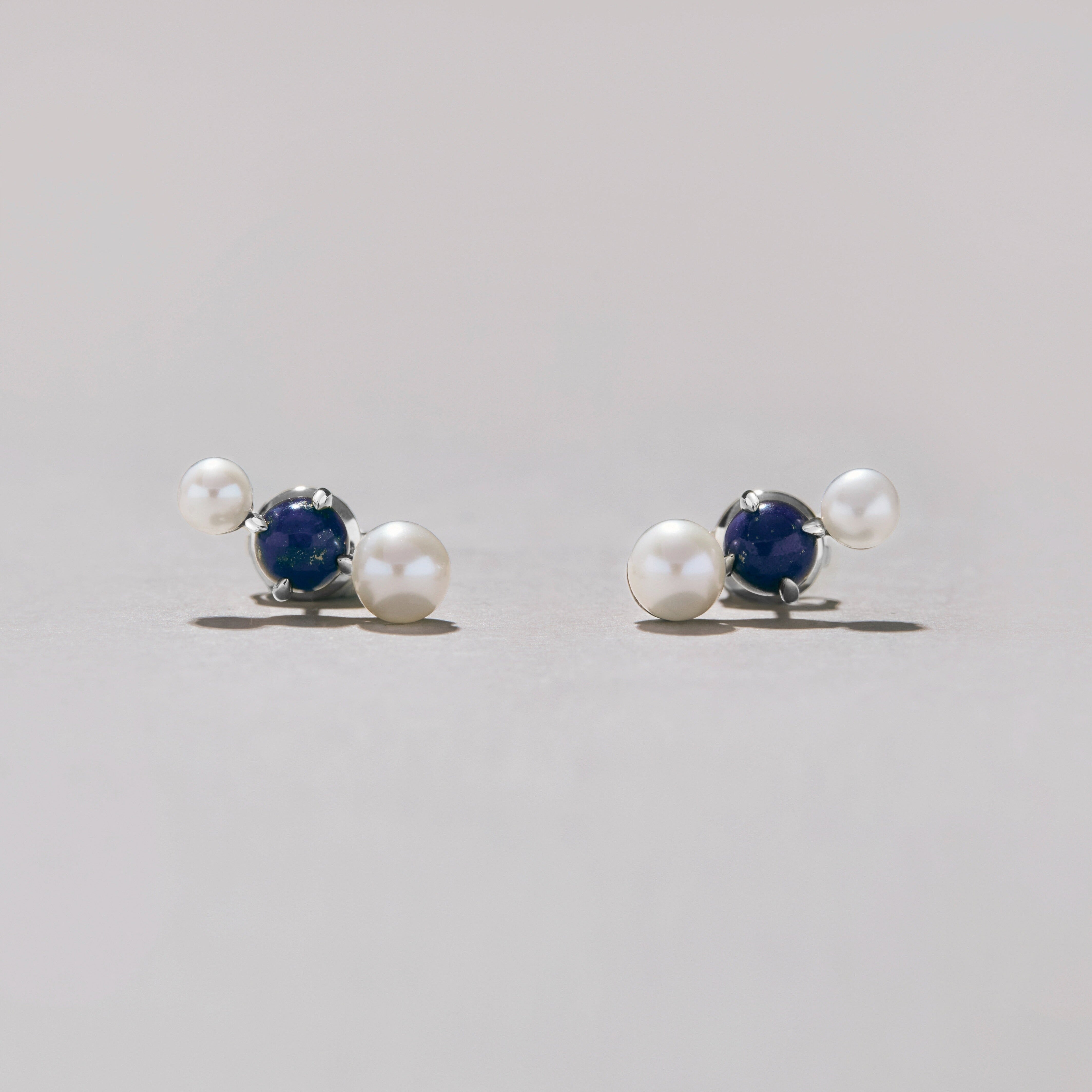 Pair of silver earrings with pearls and blue stones on a light gray background