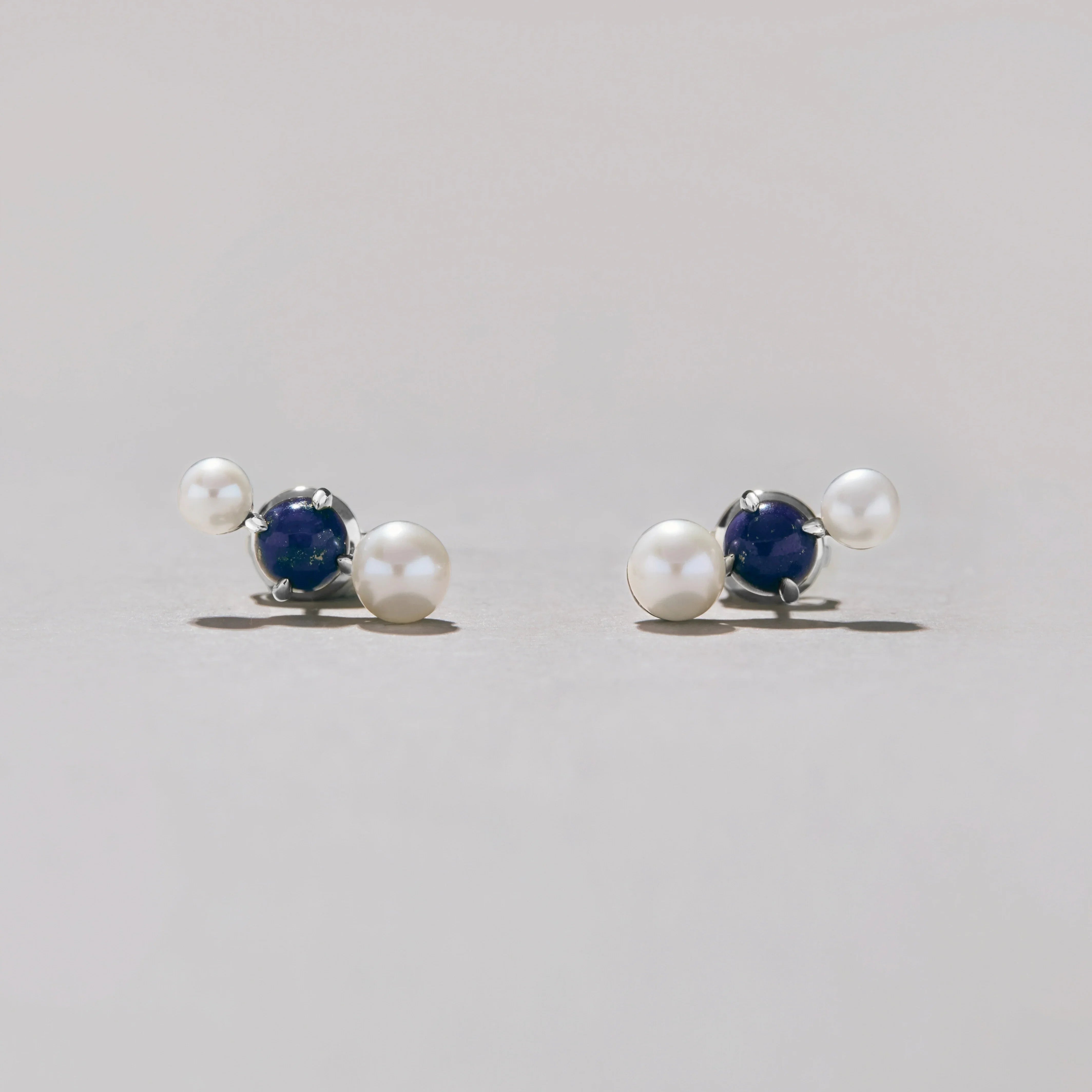 Pair of silver earrings with pearls and blue stones on a light gray background