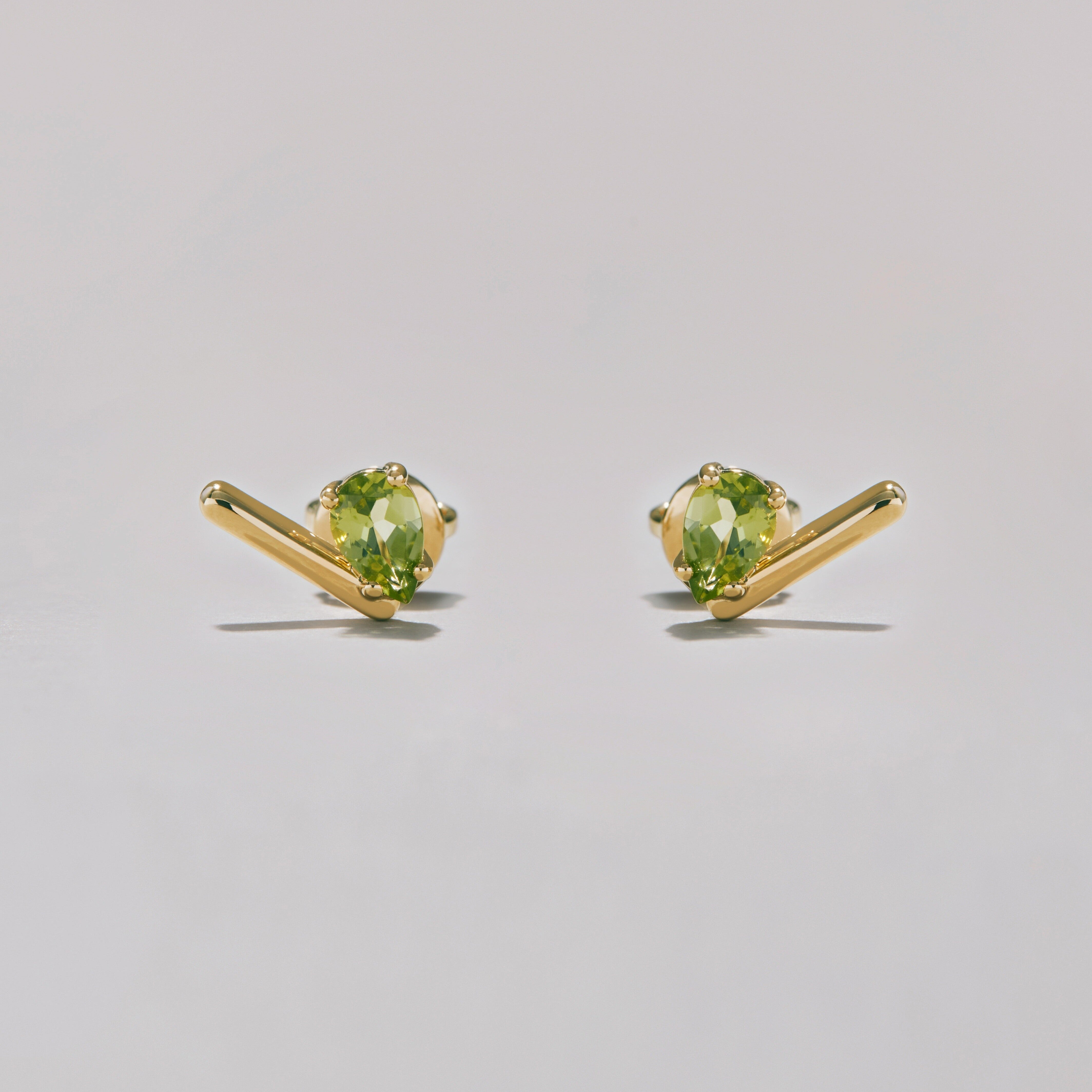 Pair of gold stud earrings with green pear-shaped gemstones on a light gray background