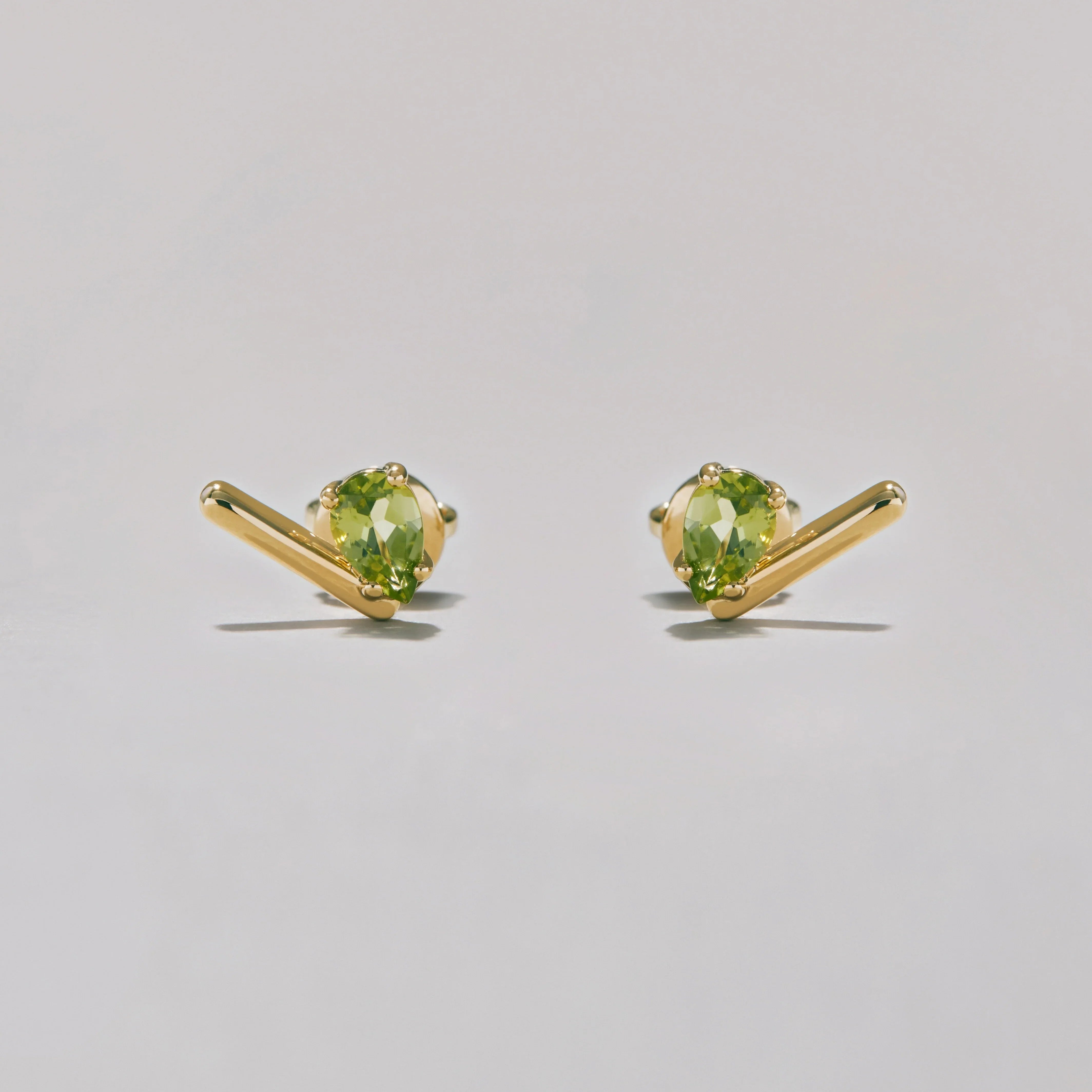 Pair of gold stud earrings with green pear-shaped gemstones on a light gray background