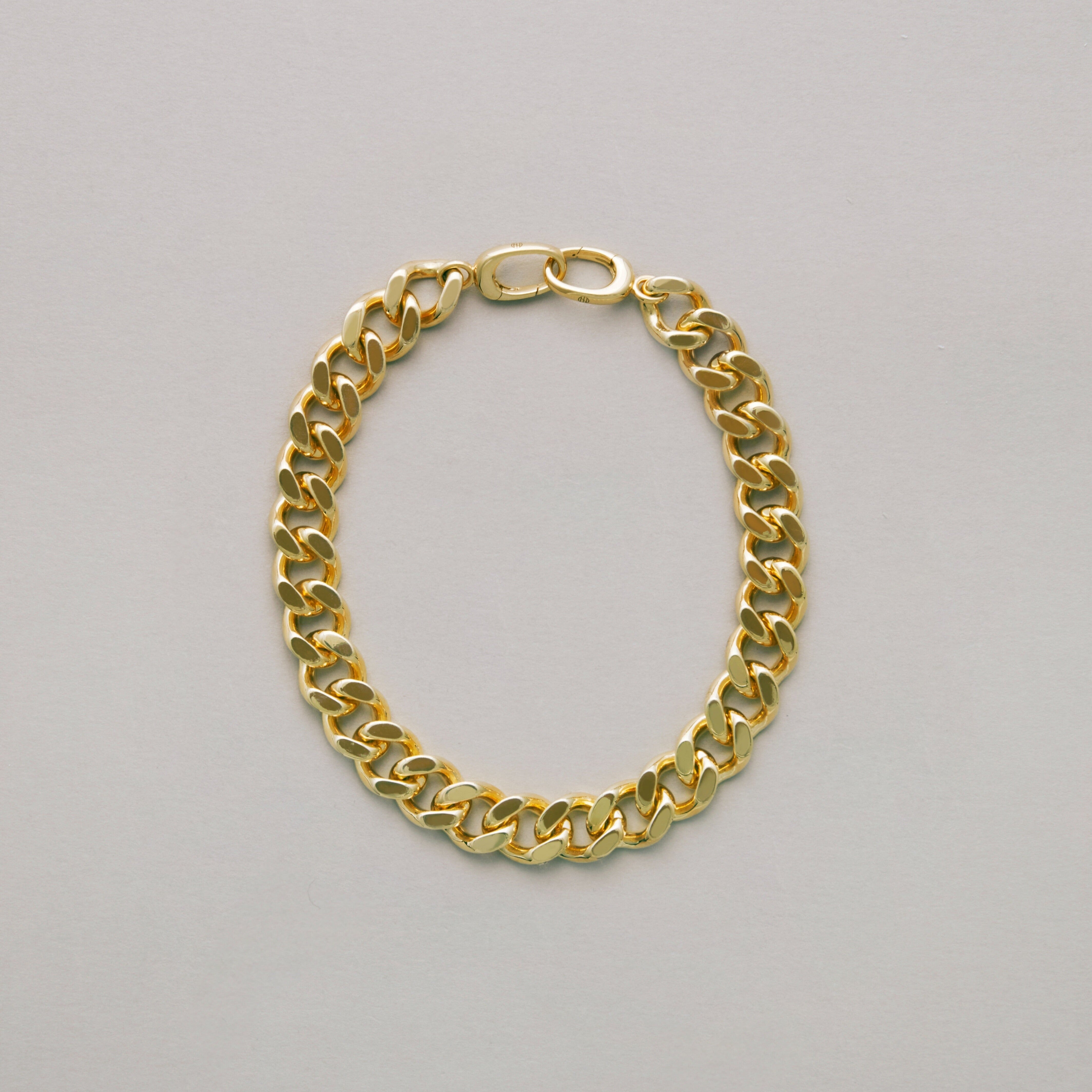 Classic gold curb chain bracelet laid flat on light surface