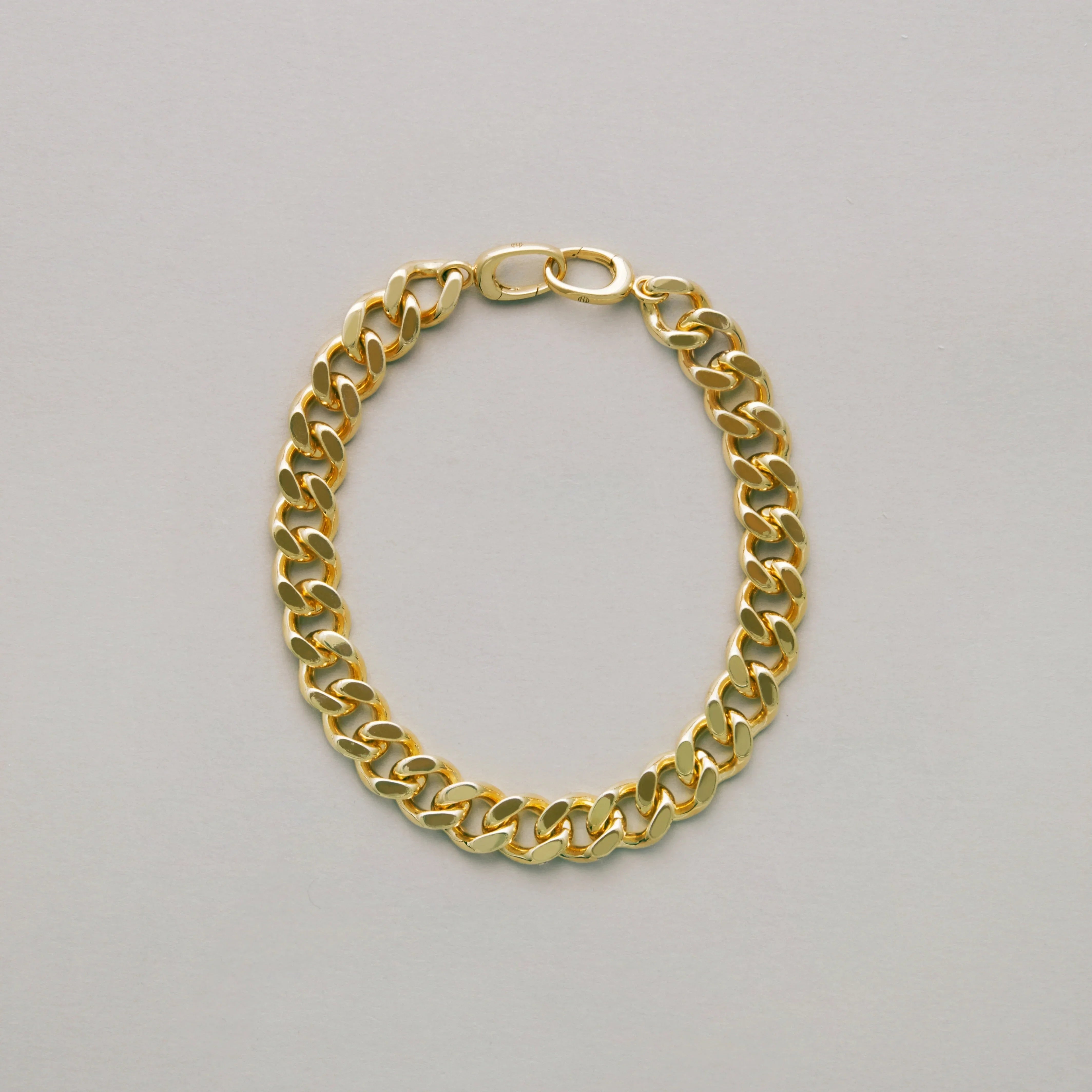 Classic gold curb chain bracelet laid flat on light surface