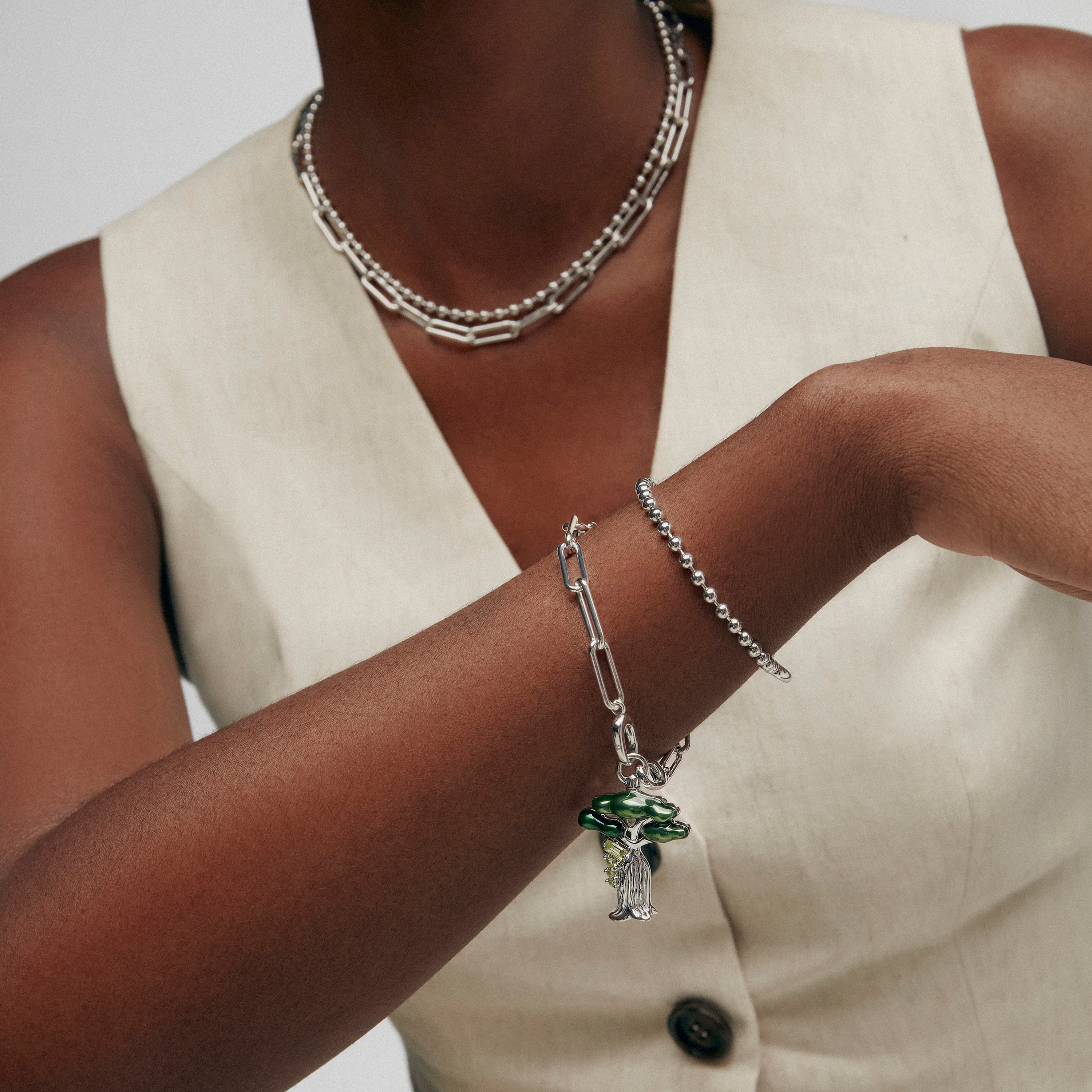 Silver paperclip chain bracelet with green enamel baobab tree charm on model's wrist.