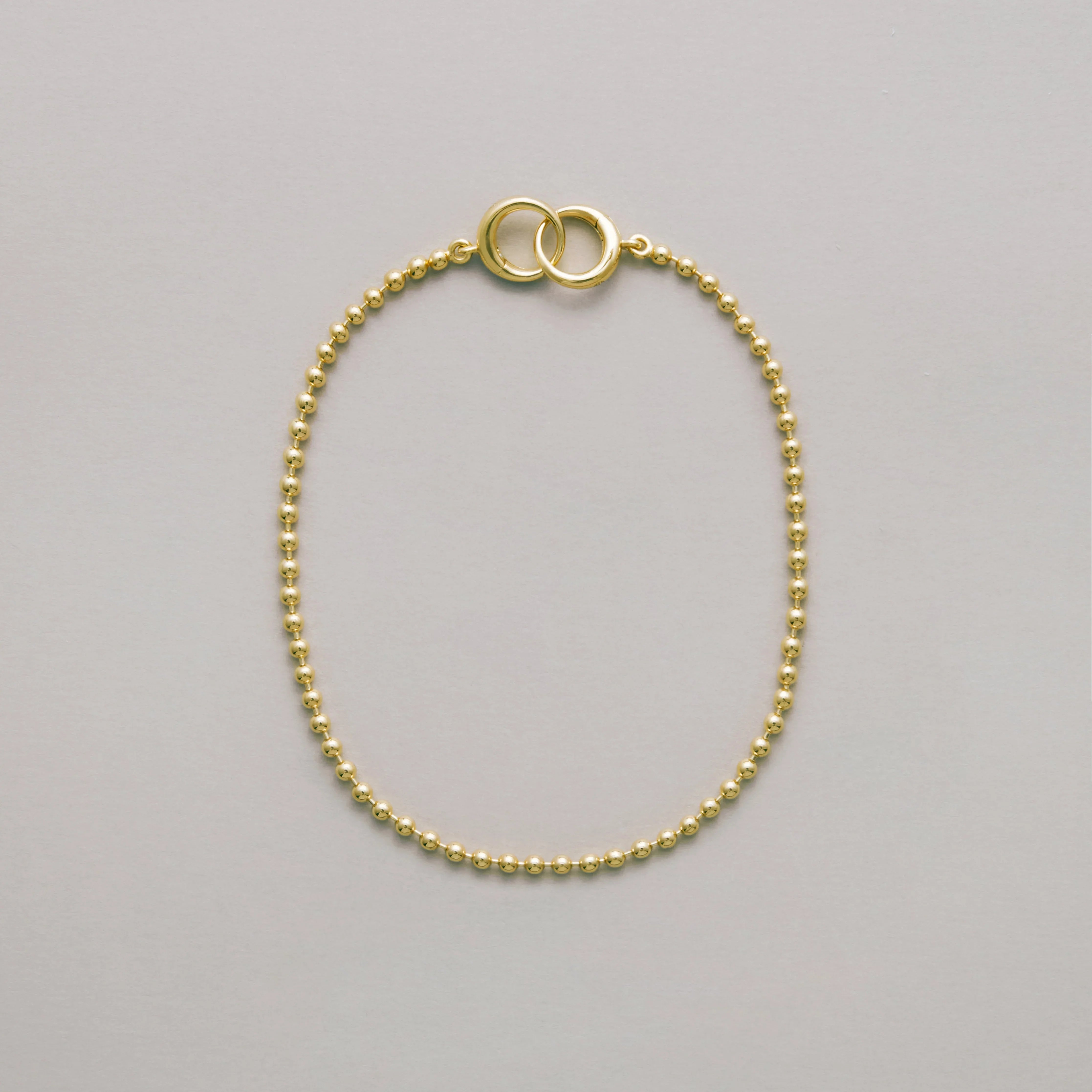 Gold beaded bracelet with interlocking loops on neutral background