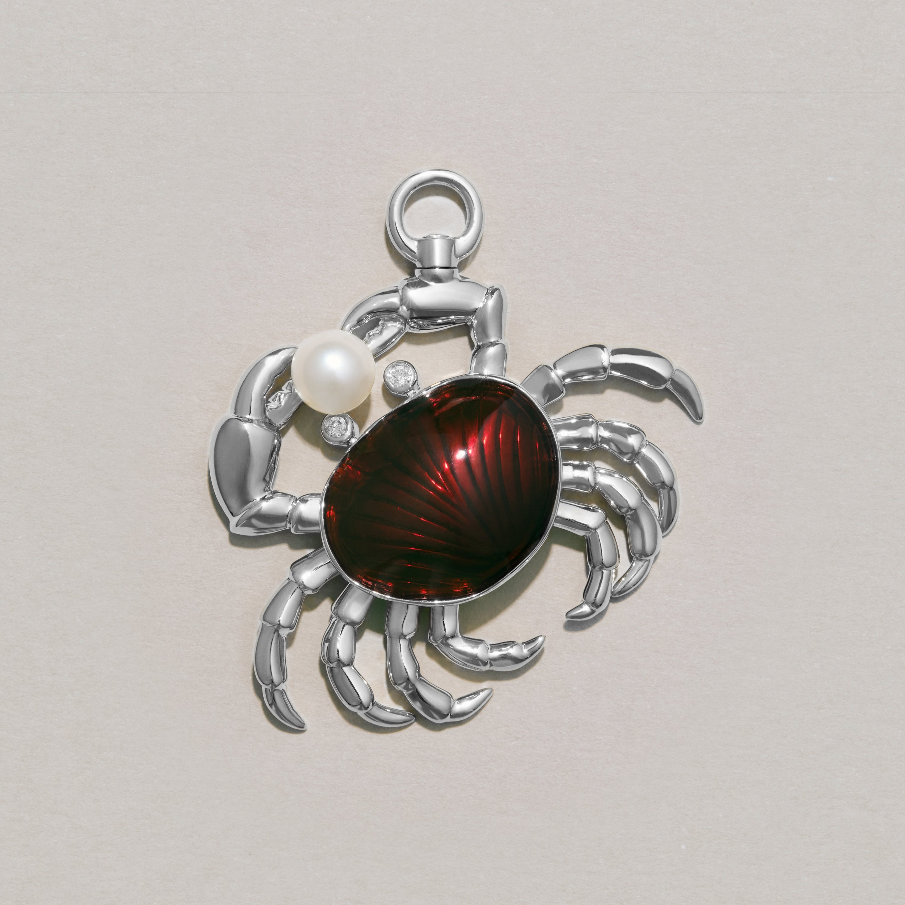Silver crab charm with red enamel and pearl on a light gray background