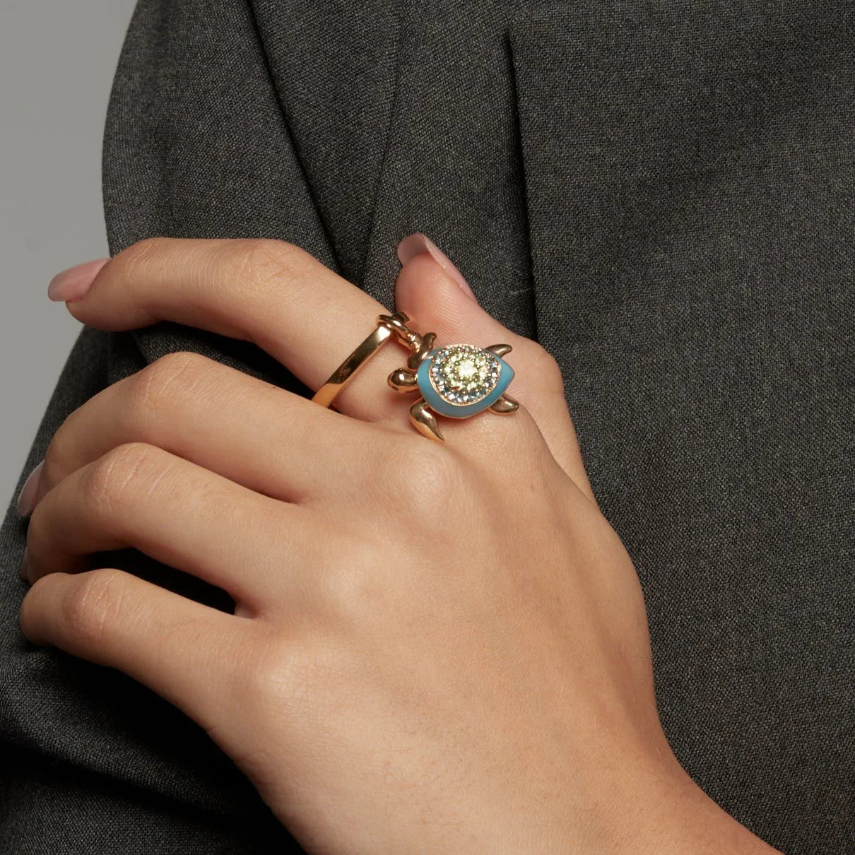 Close-up of a hand wearing a gold ring with a blue and gold turtle charm encrusted with sparkling stones.