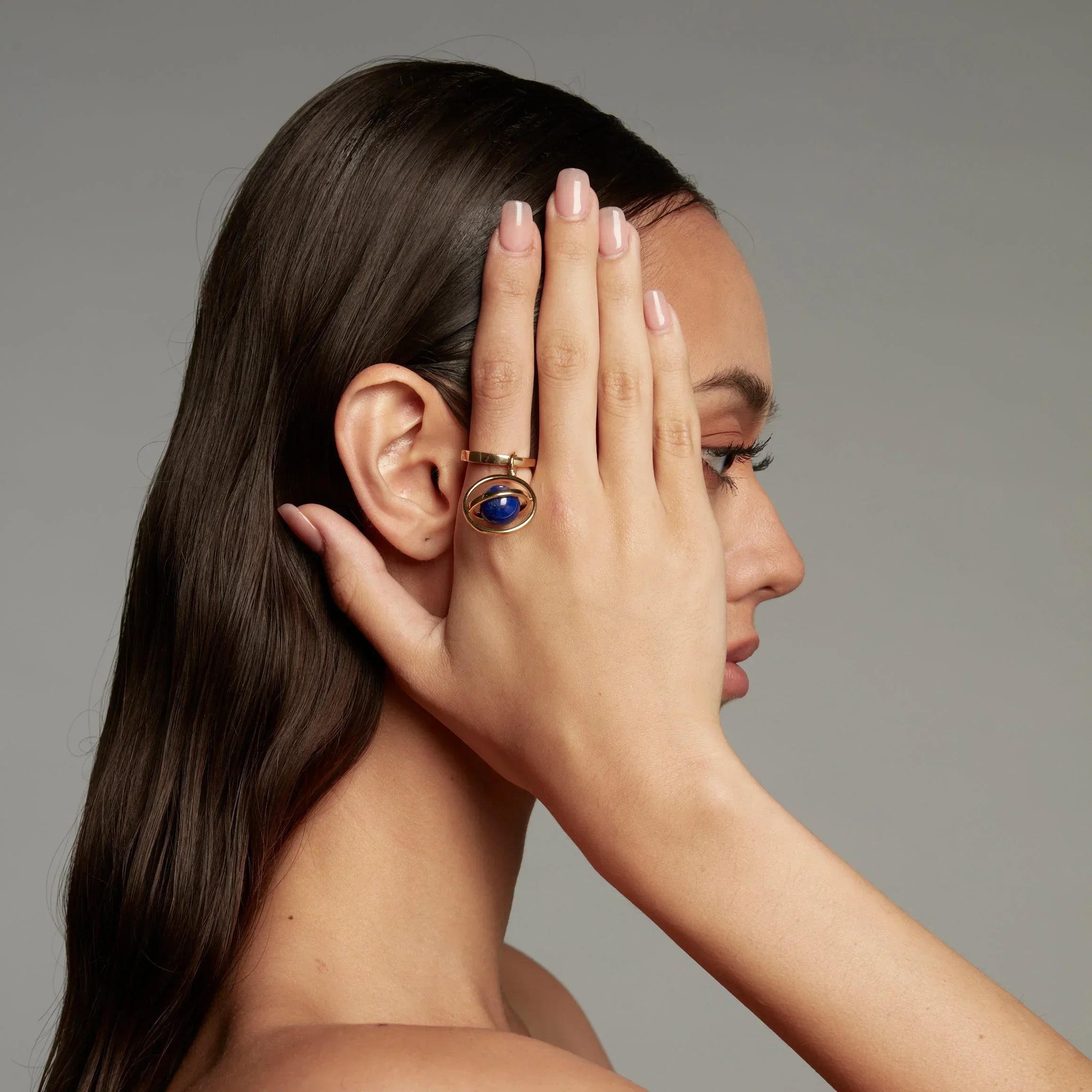 Side profile of woman wearing a bold gold ring with a lapis lazuli gemstone designed in an orbital planet-inspired setting.