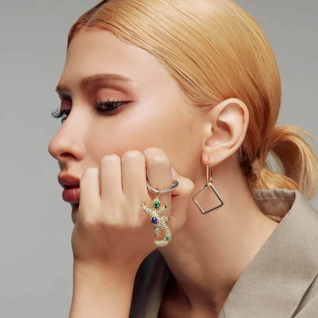 Blonde woman showcasing gold geometric hoop with lizard charm featuring green and blue stones