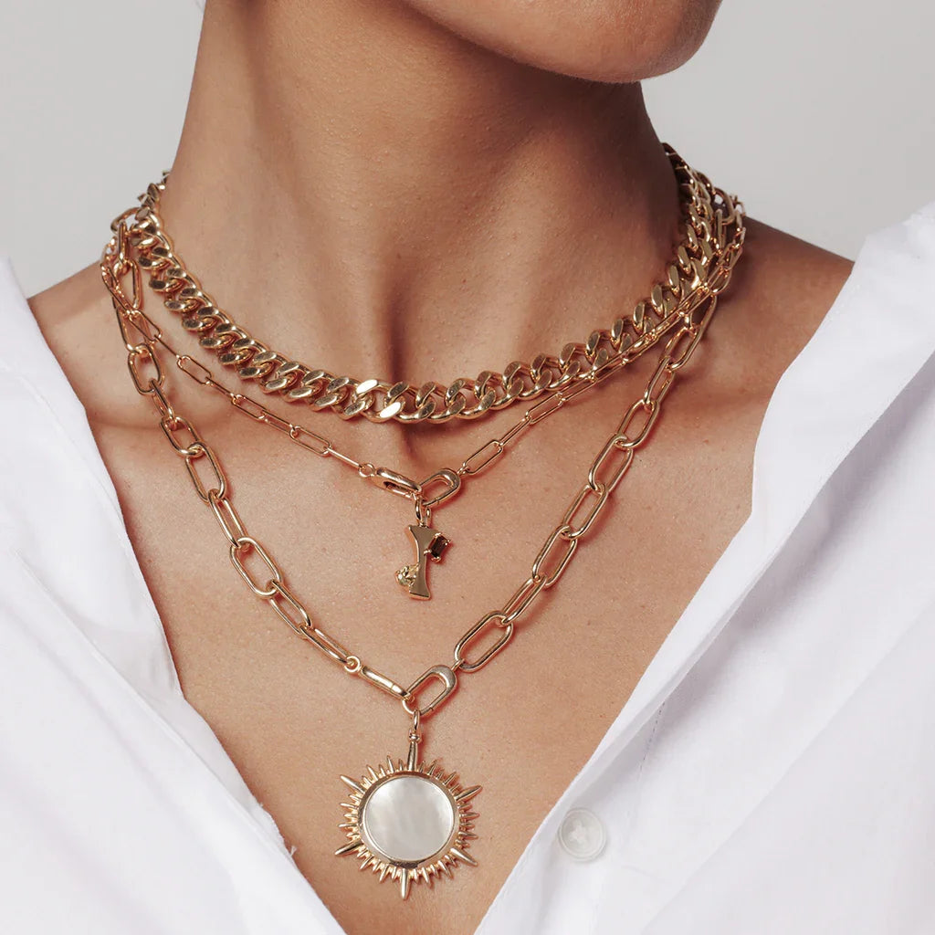 Layered gold chains with sunburst pendant featuring luminous mother-of-pearl, styled in sunlight.