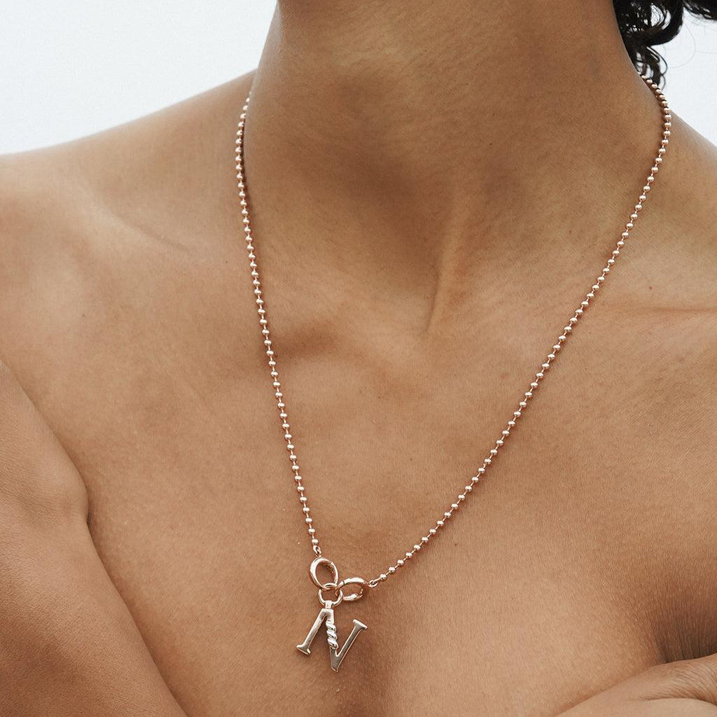 Minimalist rose gold beaded necklace with a letter charm worn on bare skin