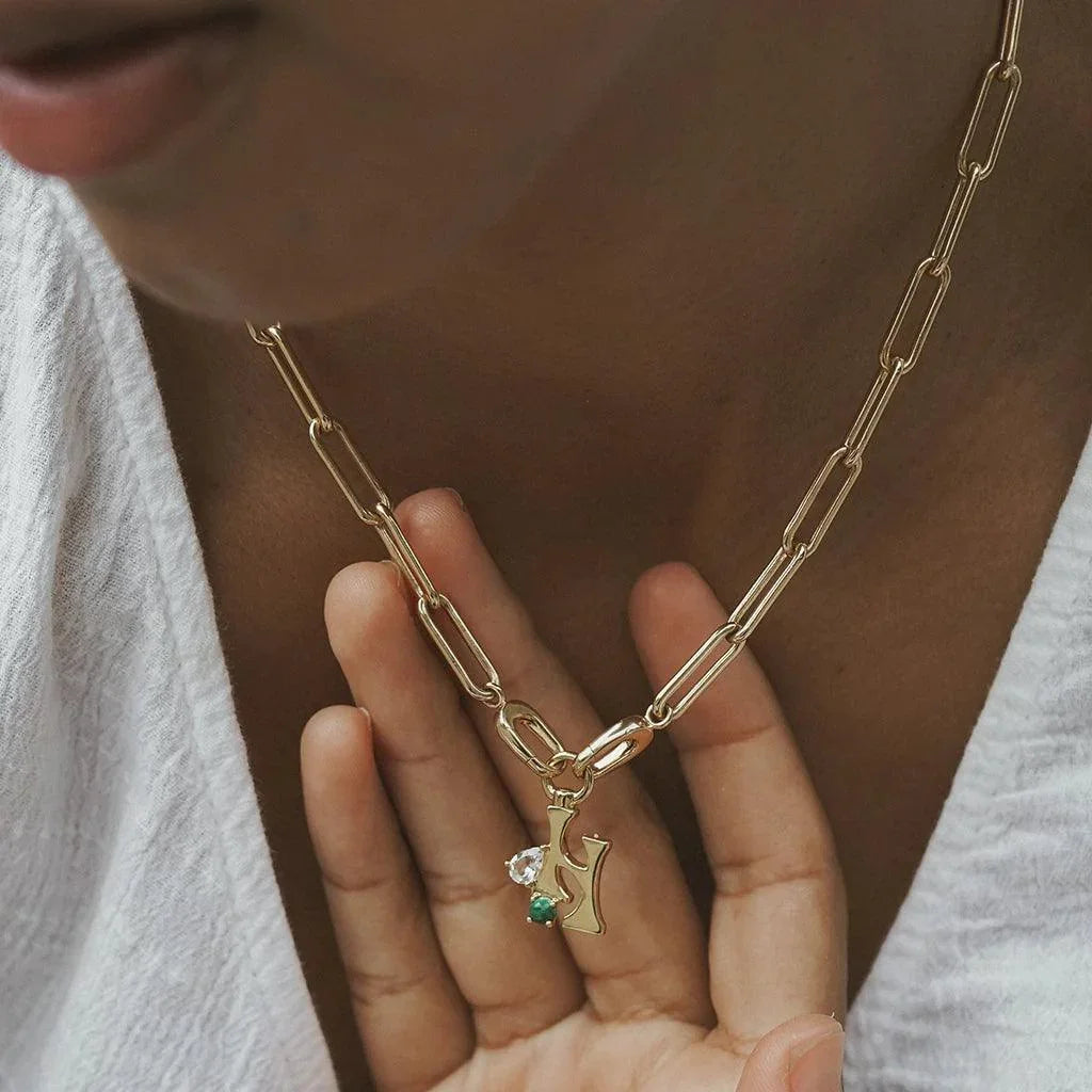 Close-up of gold chain necklace with personalized letter and gemstone charms.