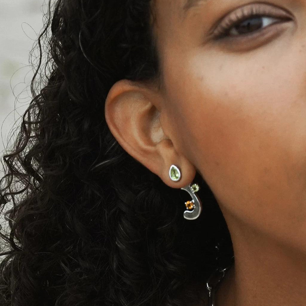 Close-up of a woman's ear wearing the teardrop-shaped green gemstone stud earring with a silver and gemstone-accented detachable drop charm below.