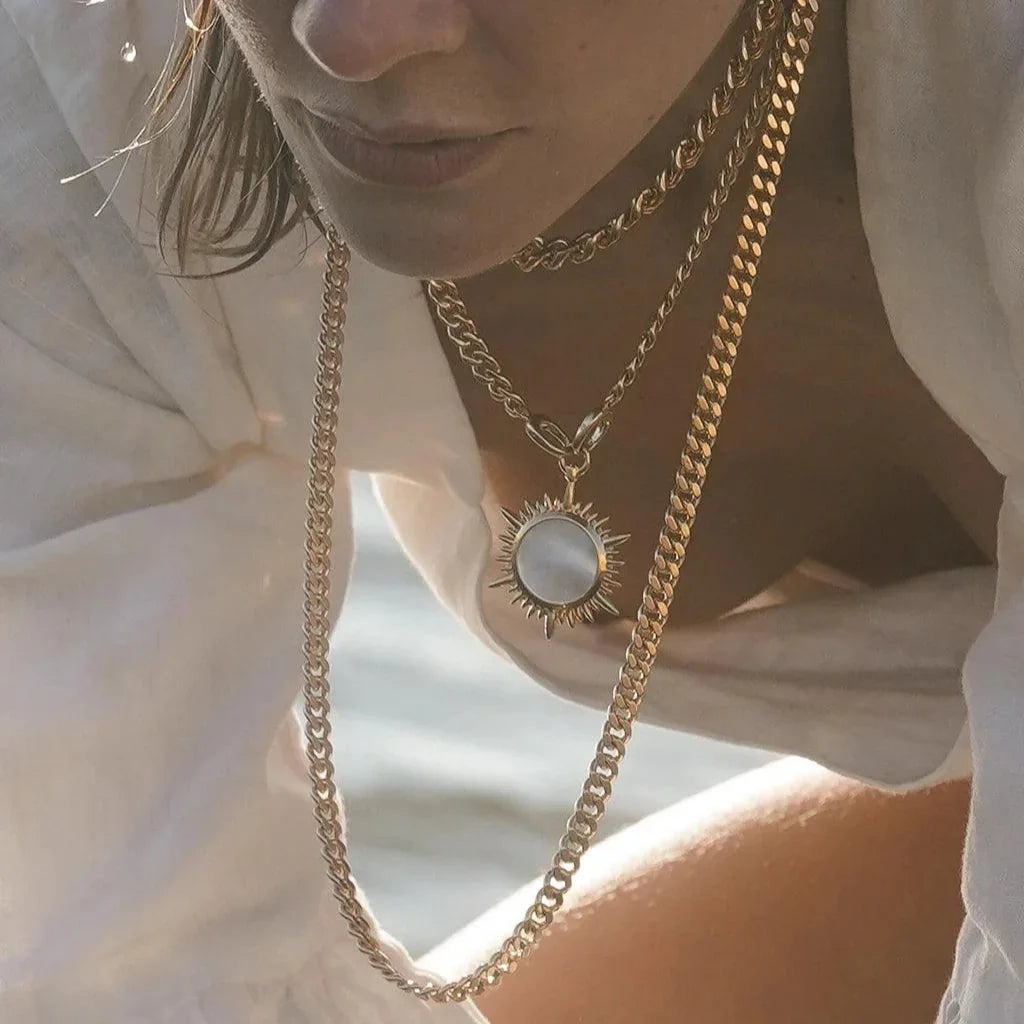 Statement gold sun charm necklace layered with chunky and link chains for a bold, elegant look.