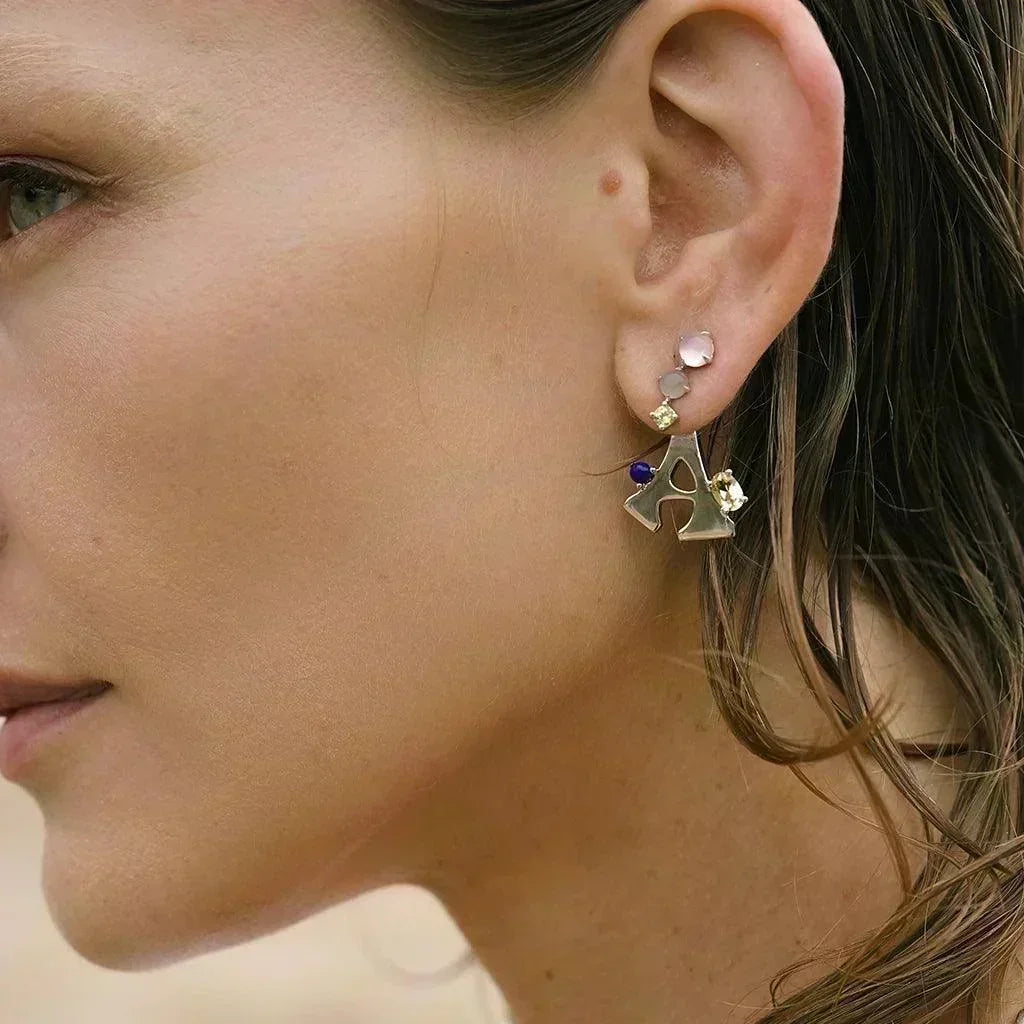 Side view of woman wearing a silver letter A earring accented with colorful gemstones.