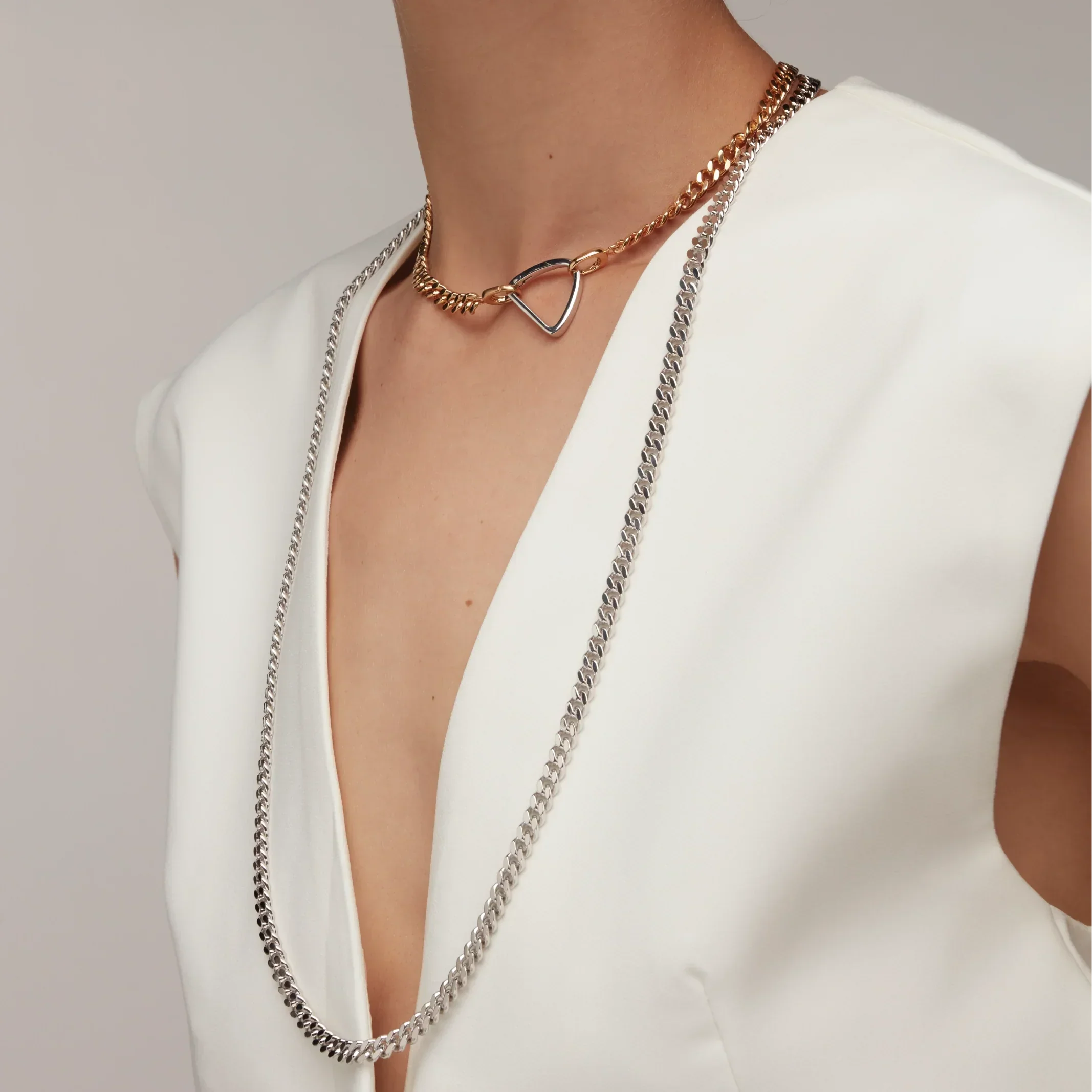 Dual-tone gold and silver necklaces styled together, featuring a geometric charm and long silver chain.