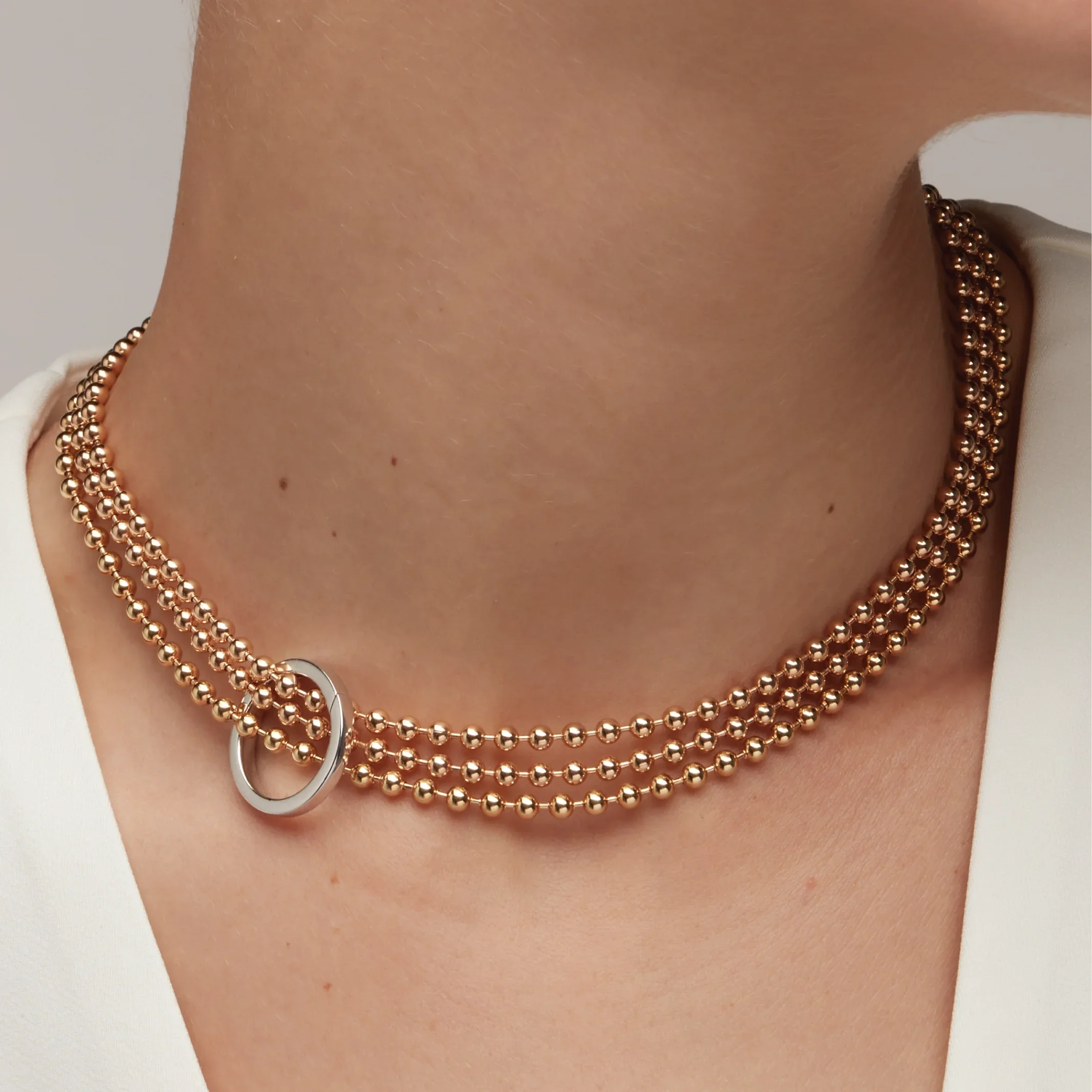 Triple-layer gold beaded choker with silver ring centerpiece on woman's neck in white top