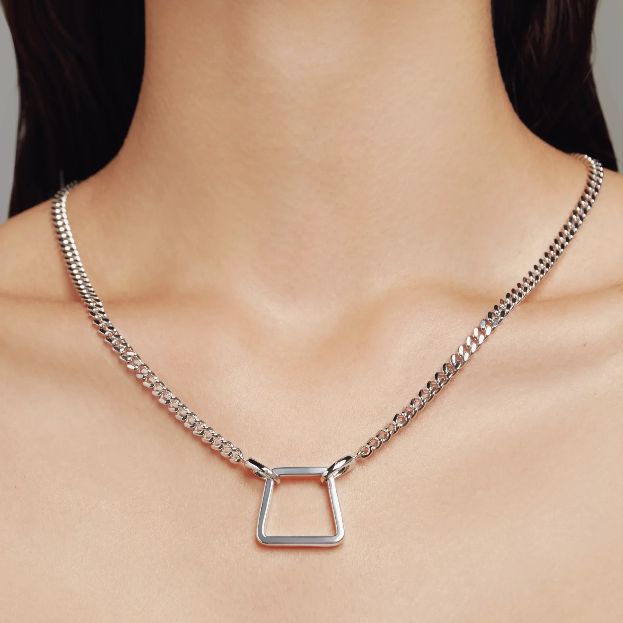 Woman wearing silver curb chain necklace with geometric center pendant.