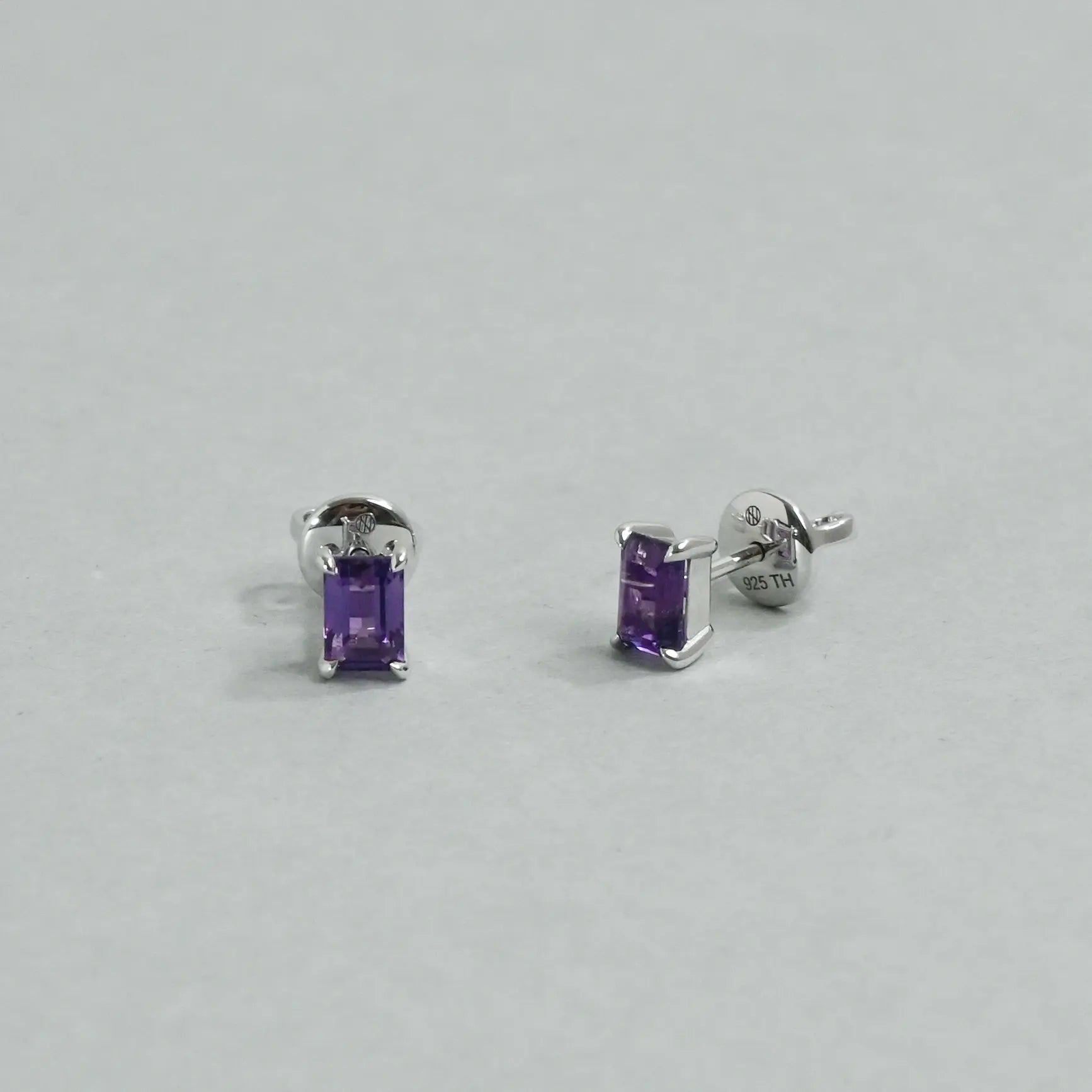 Pair of silver earrings with purple gemstones on a light gray background