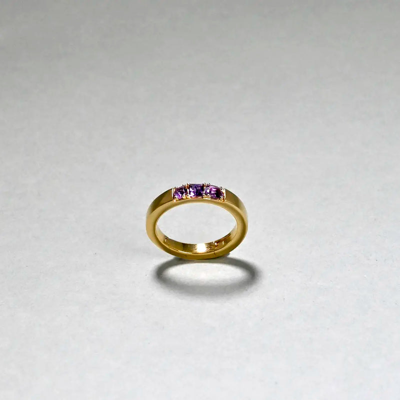 Gold ring with purple gemstones on a light gray background