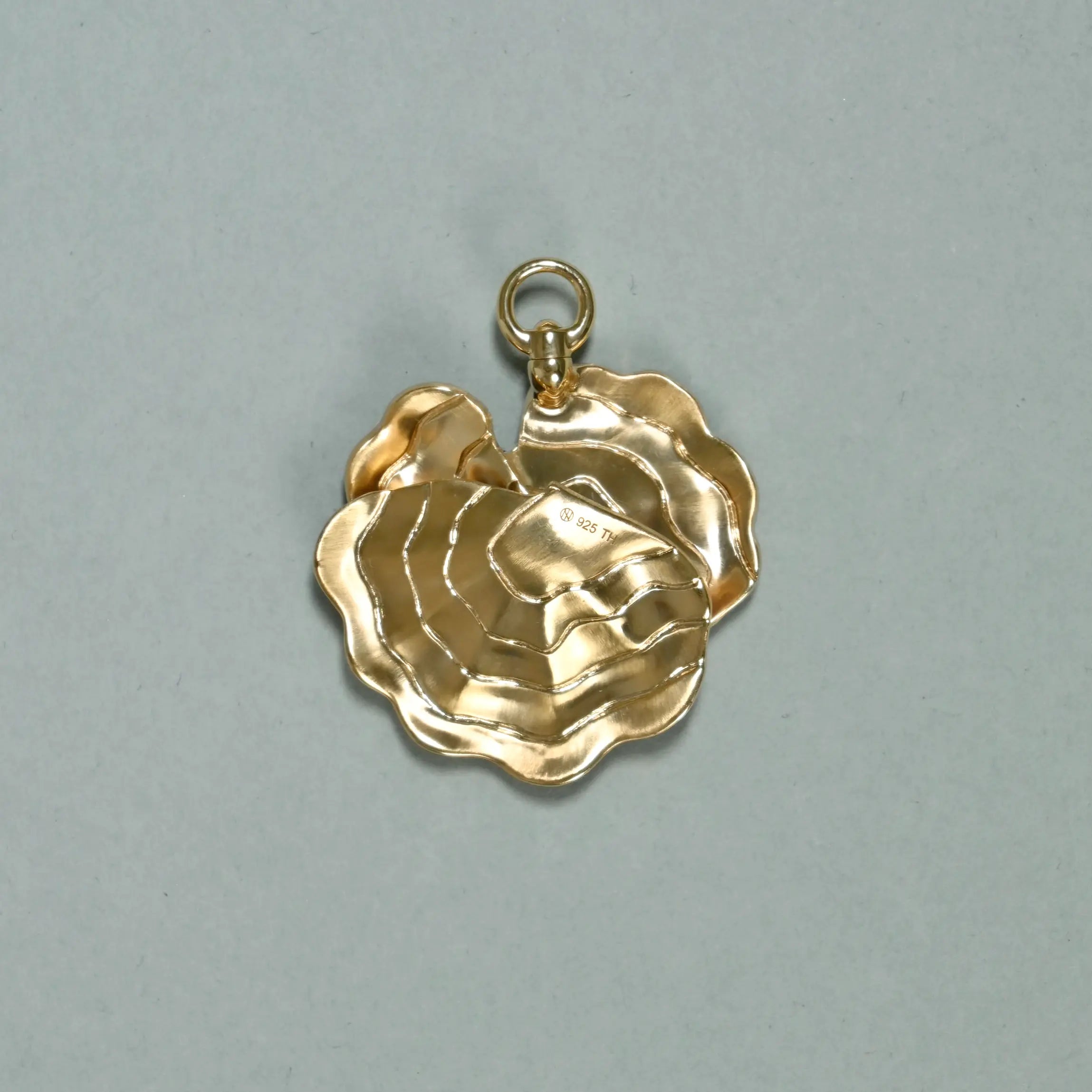 Back side of a gold rose-shaped pendant on a gray background