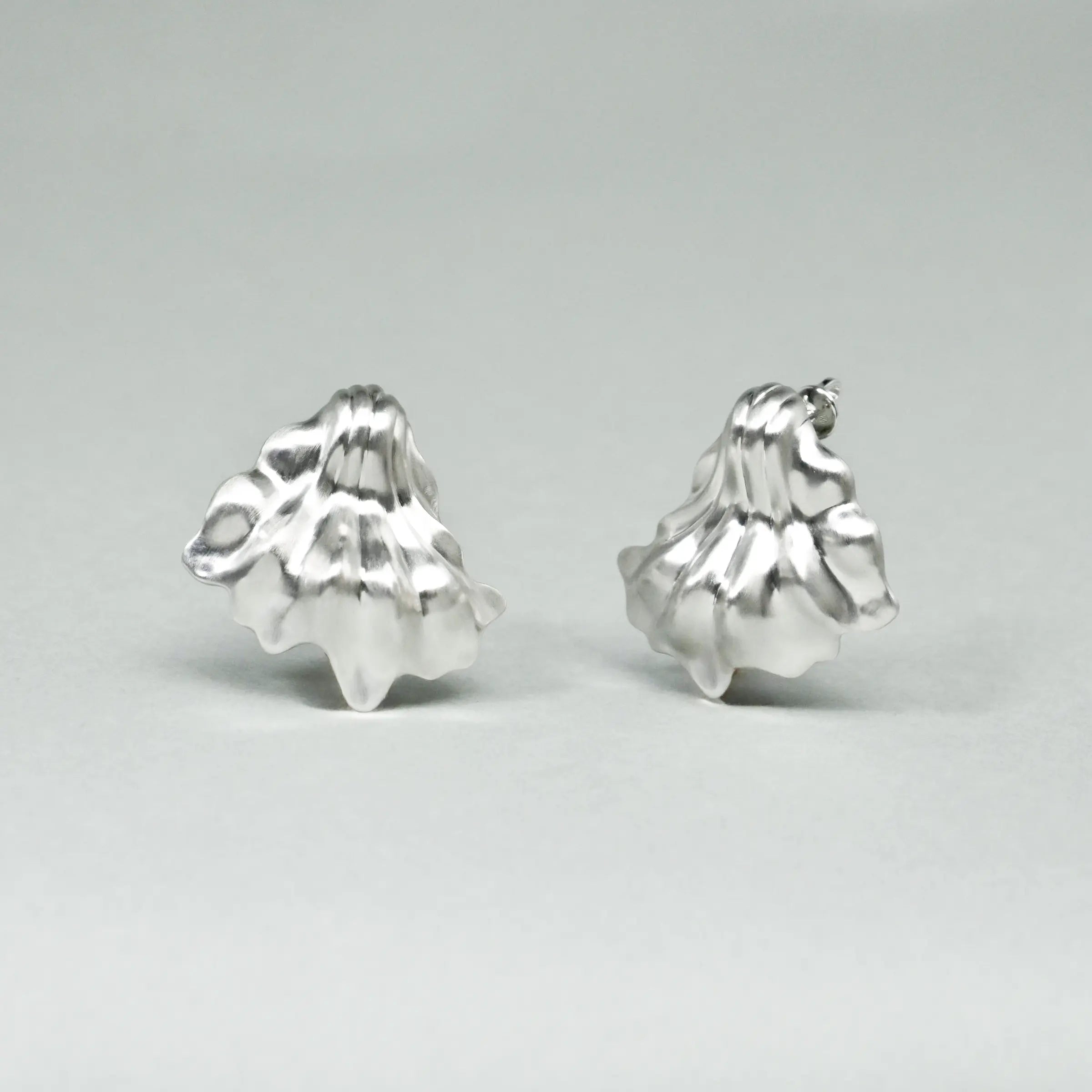 Pair of silver leaf-shaped earrings on a light gray background