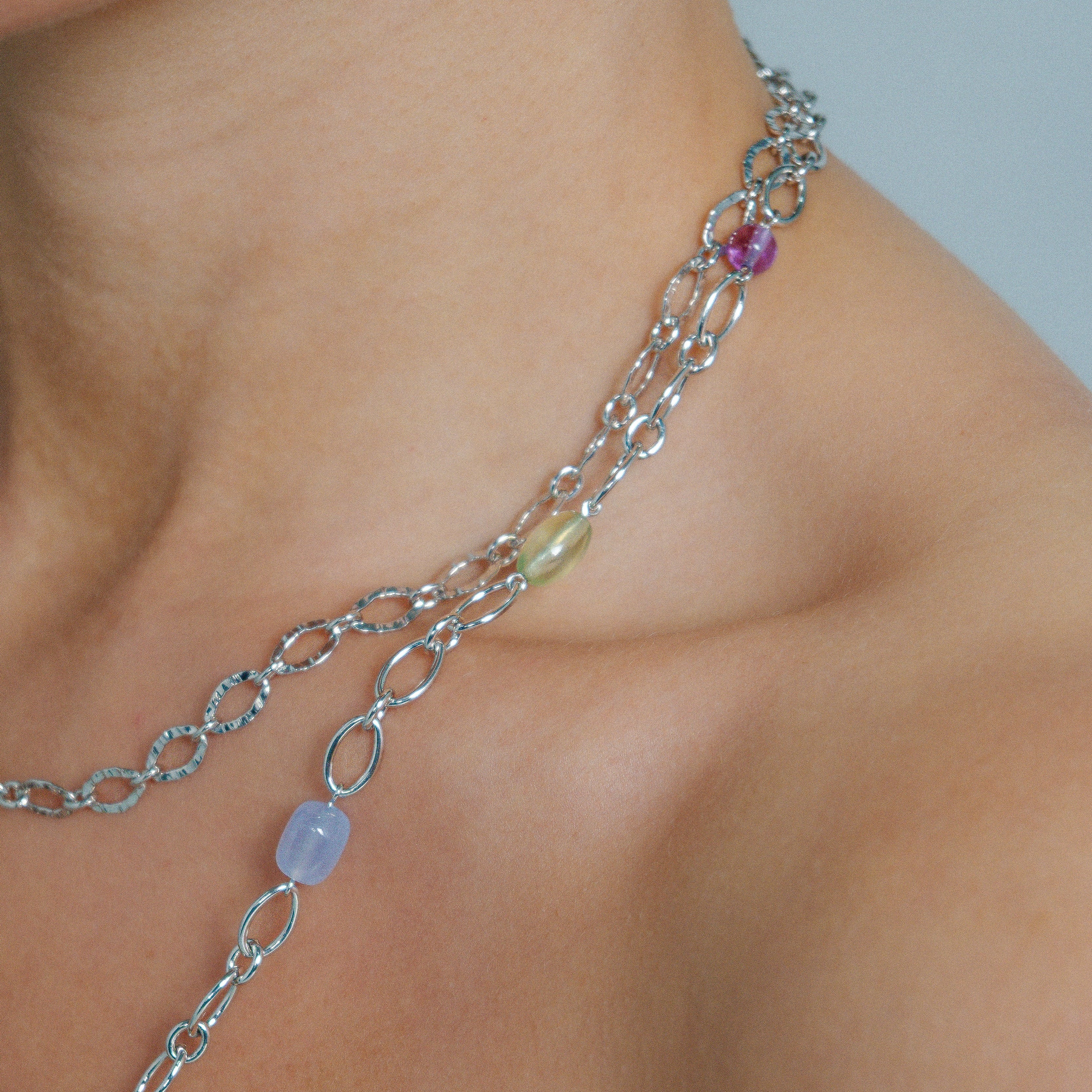 Close-up of a silver chain necklace with gemstones on a person's neck.