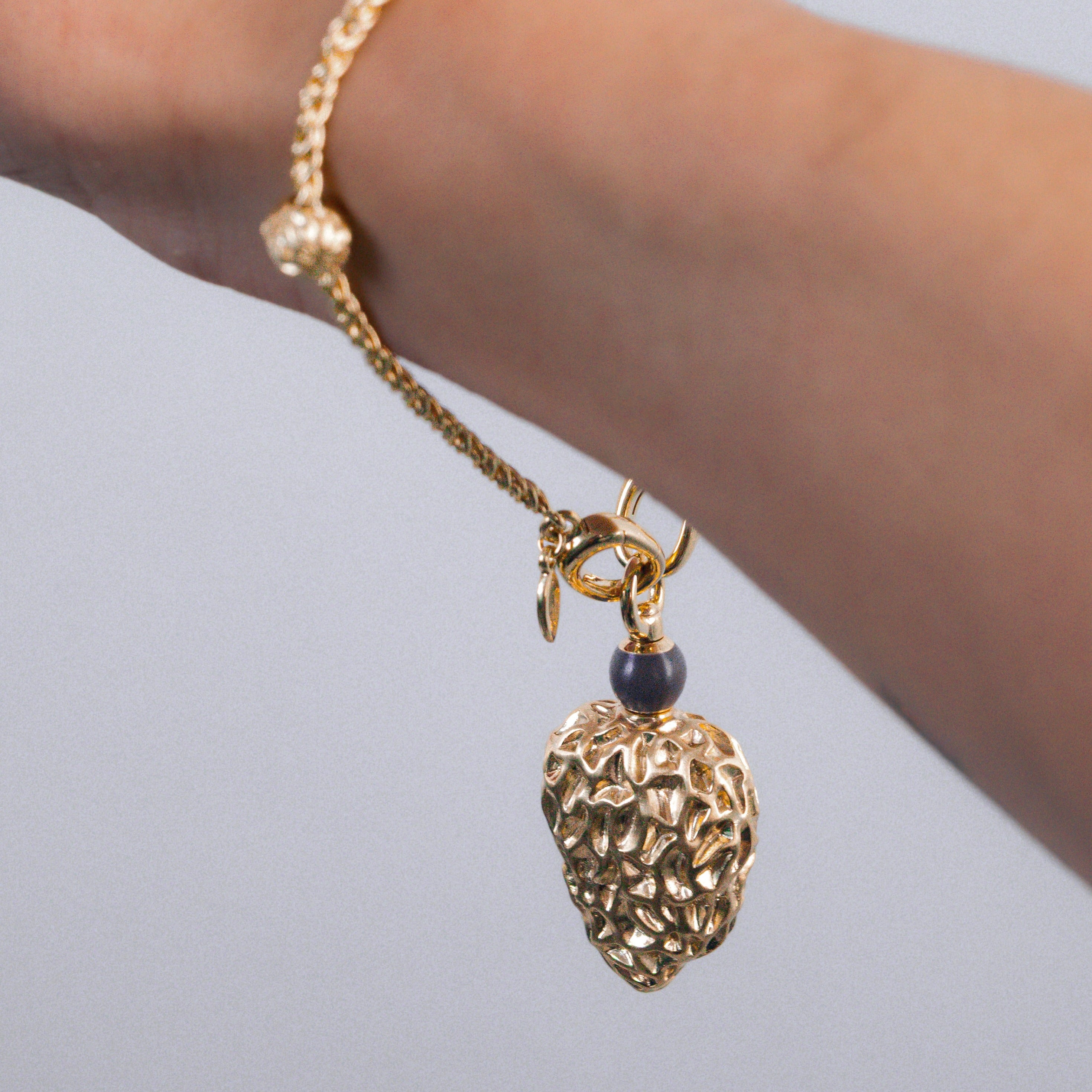 Gold bracelet with a heart-shaped pendant on a wrist against a light background