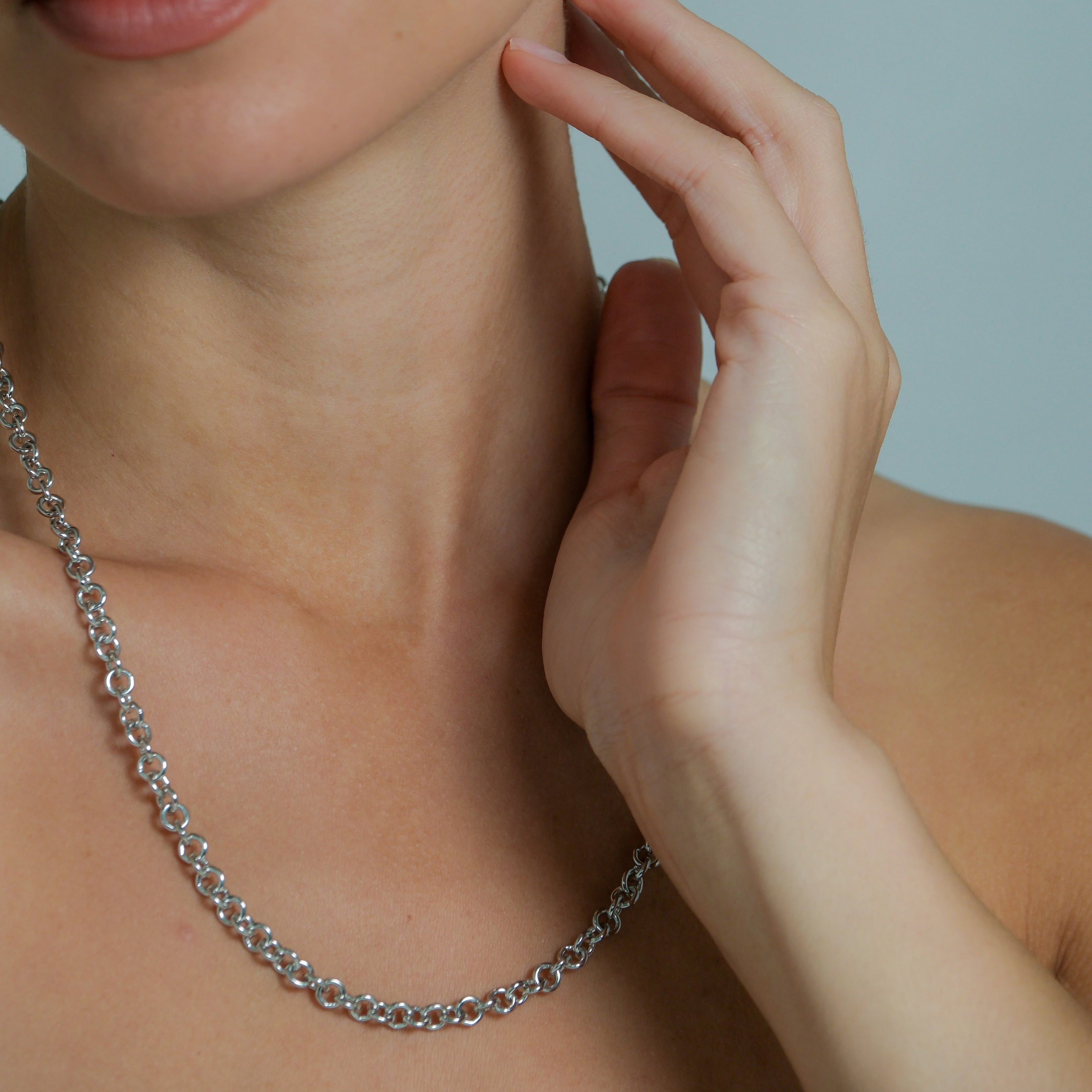 Close-up of a woman wearing silver necklace against a neutral background