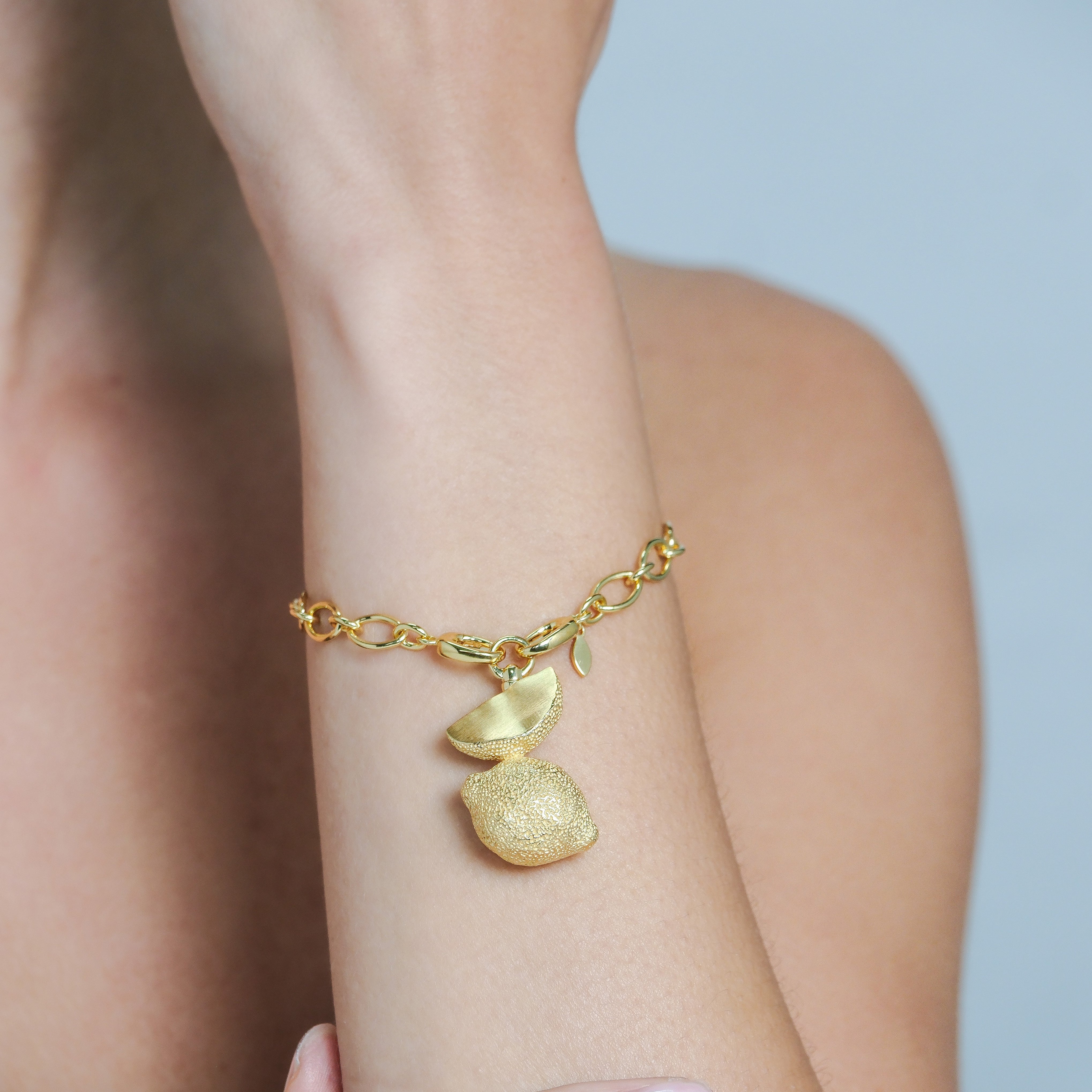 Gold bracelet with a charm on a person's wrist against a neutral background