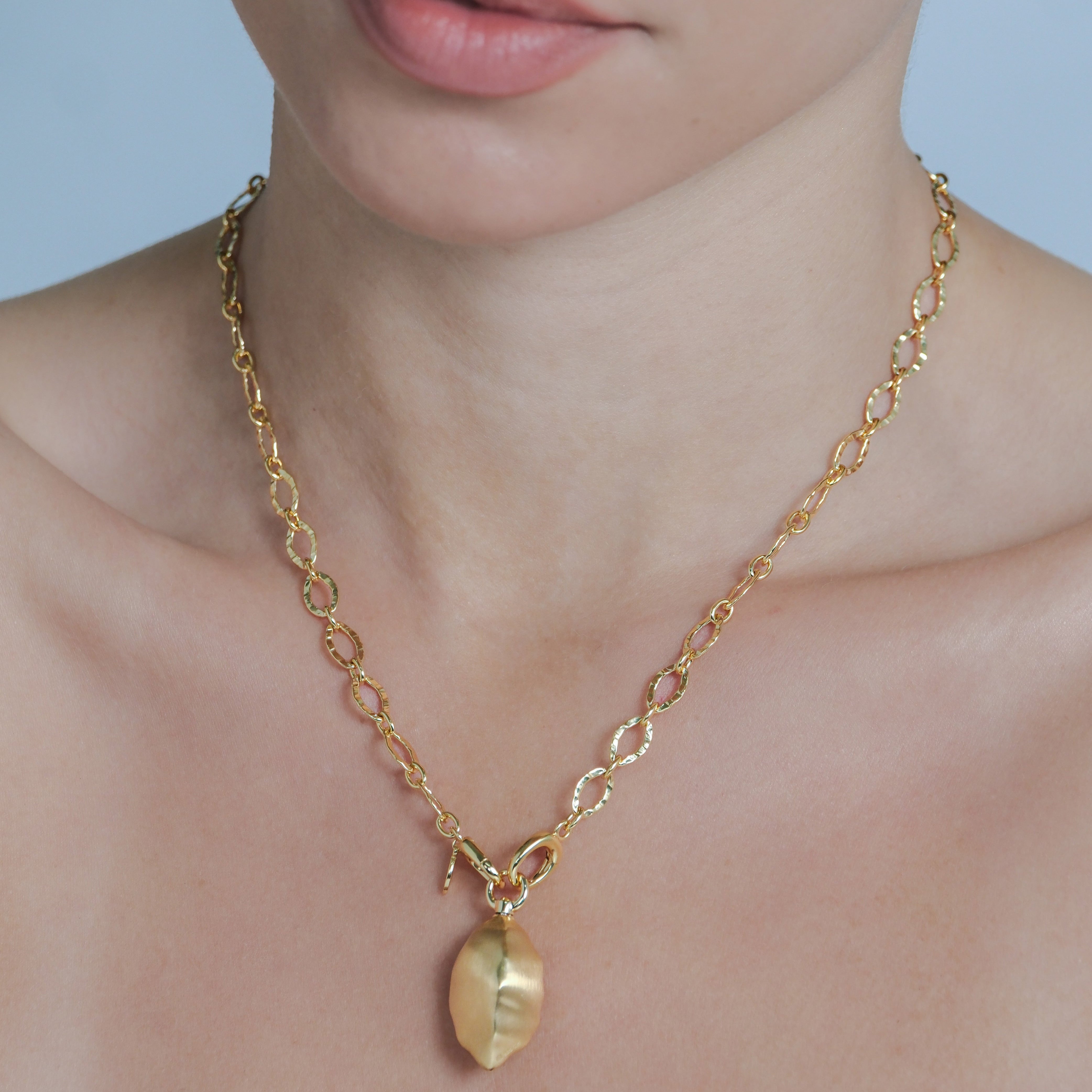 Gold necklace with a pendant worn by a person against a light blue background